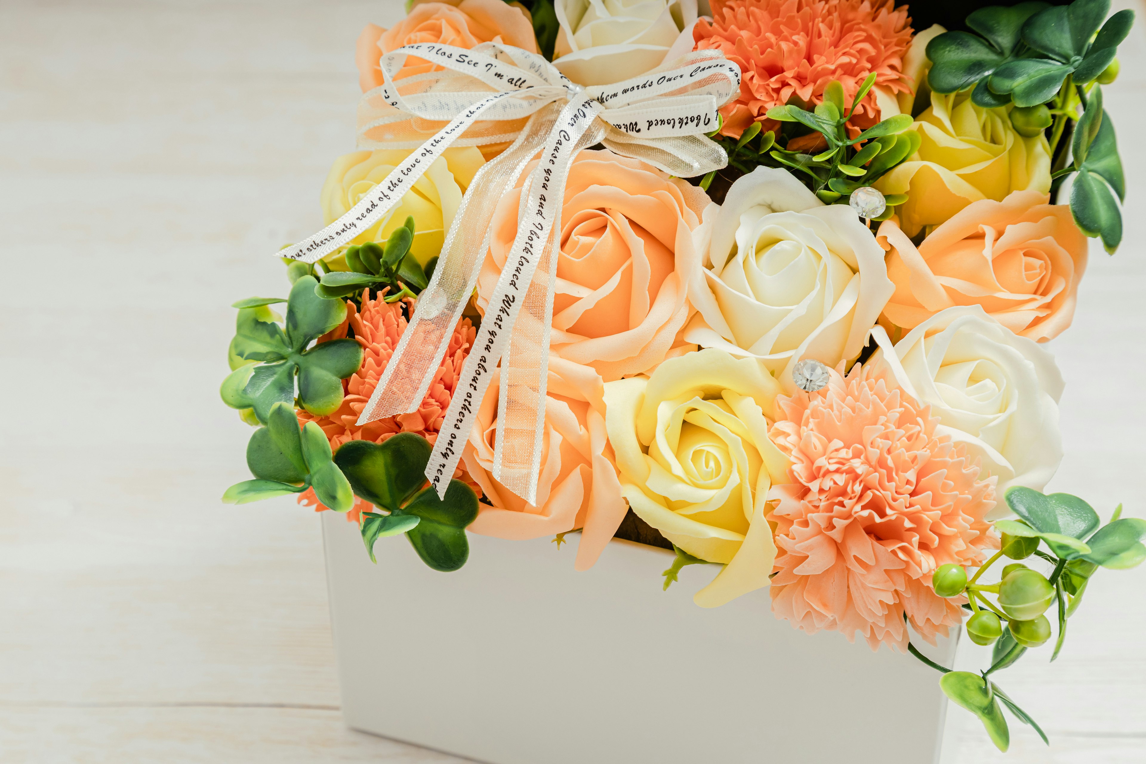 A box of roses in orange and yellow with white flowers adorned with a ribbon