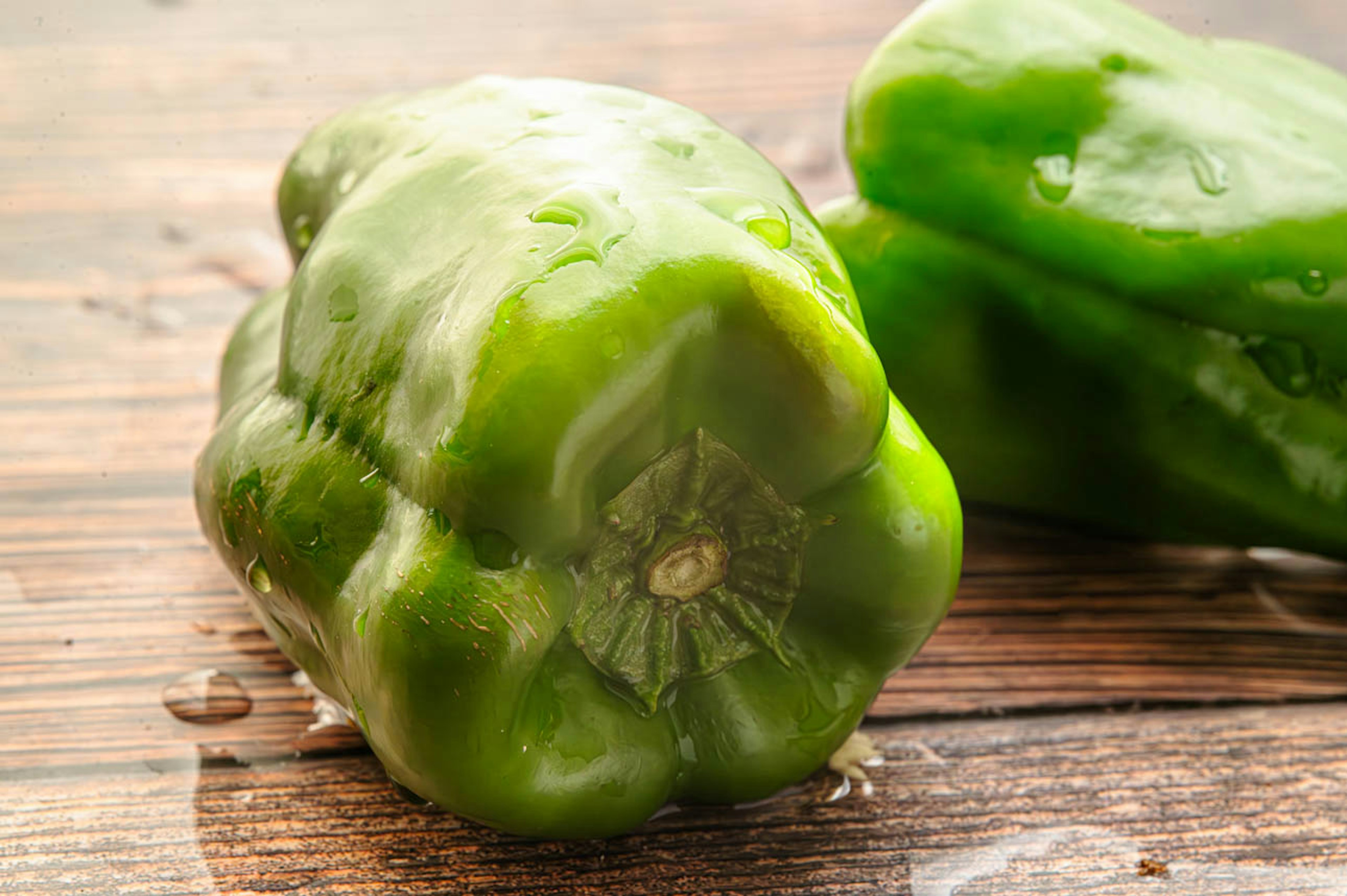 Fresh green bell peppers resting on a wooden table