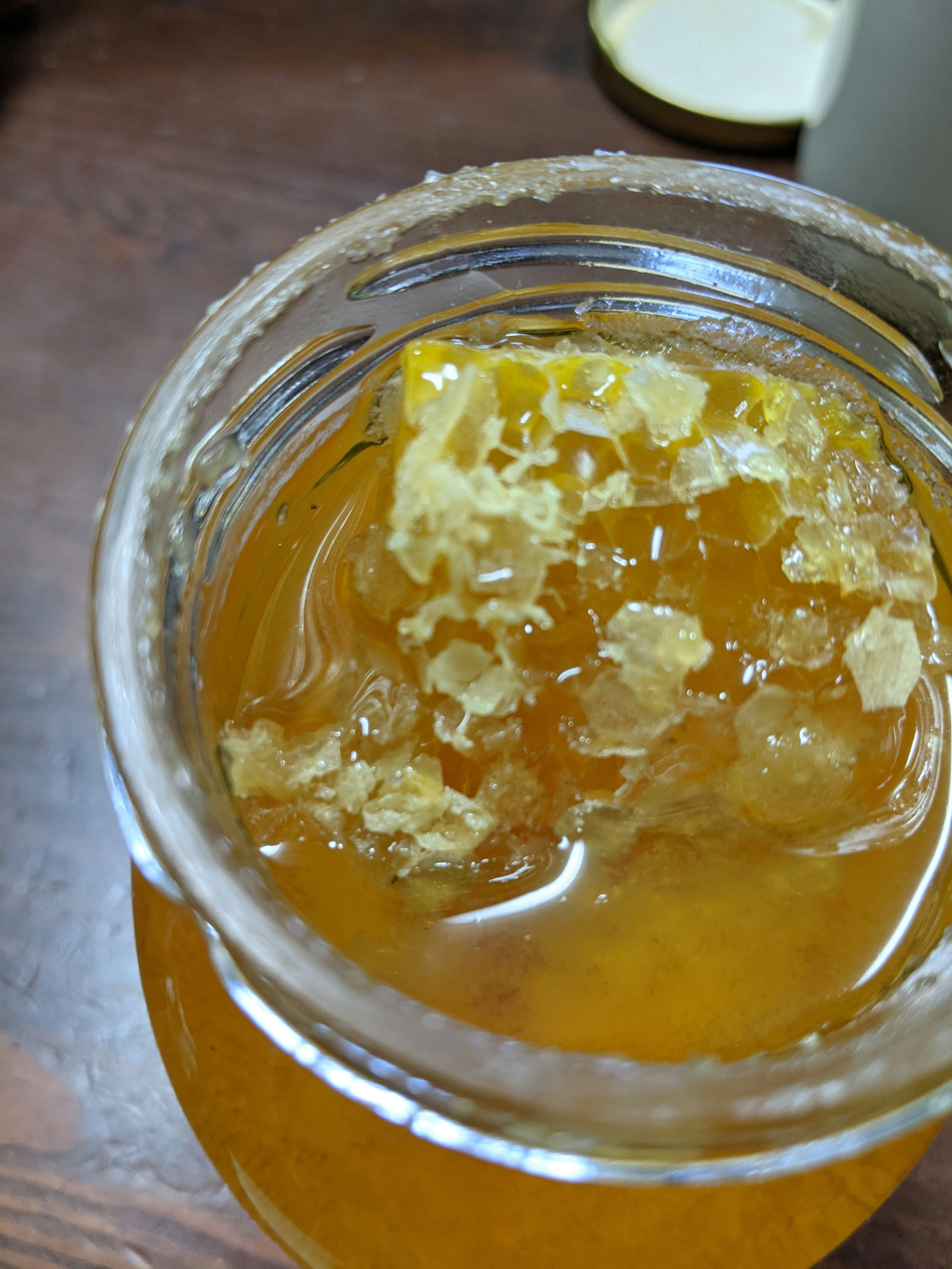 Thick yellow honey with wax chunks in a clear jar