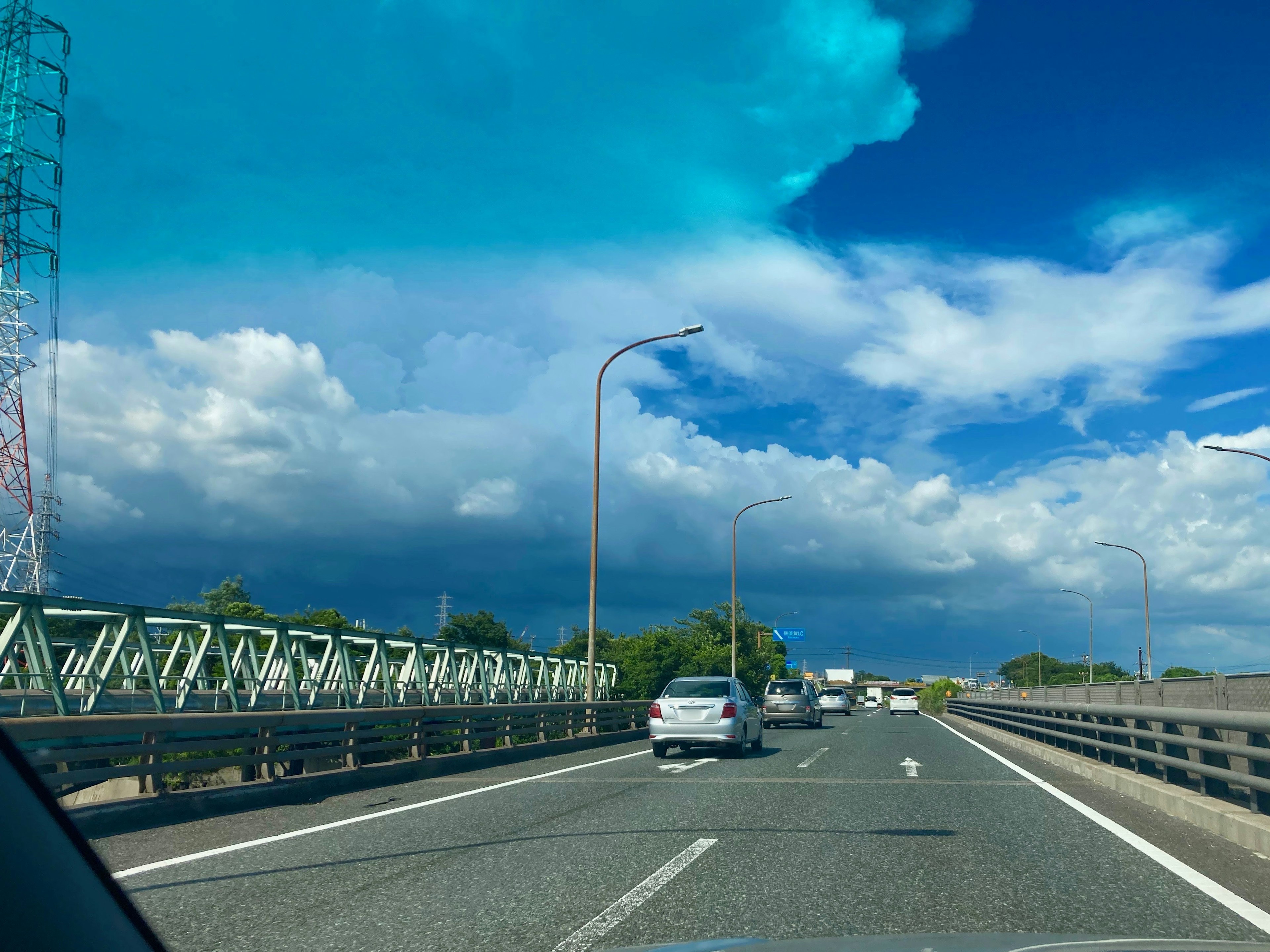 Pemandangan jalan tol dengan langit biru dan awan mobil melaju dan menara transmisi terlihat