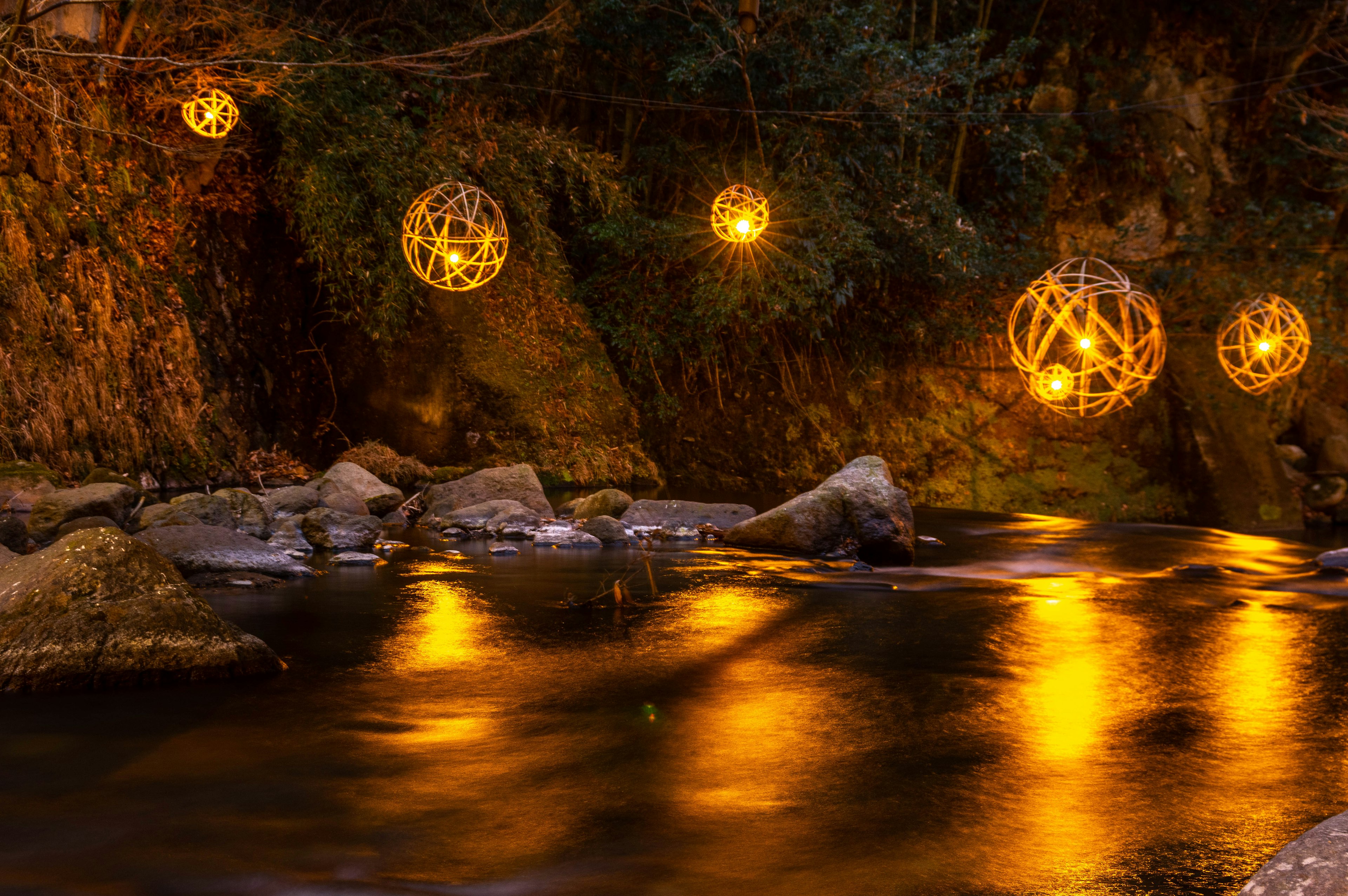 Lámparas esféricas decorativas que emiten luz cálida cerca de un río tranquilo