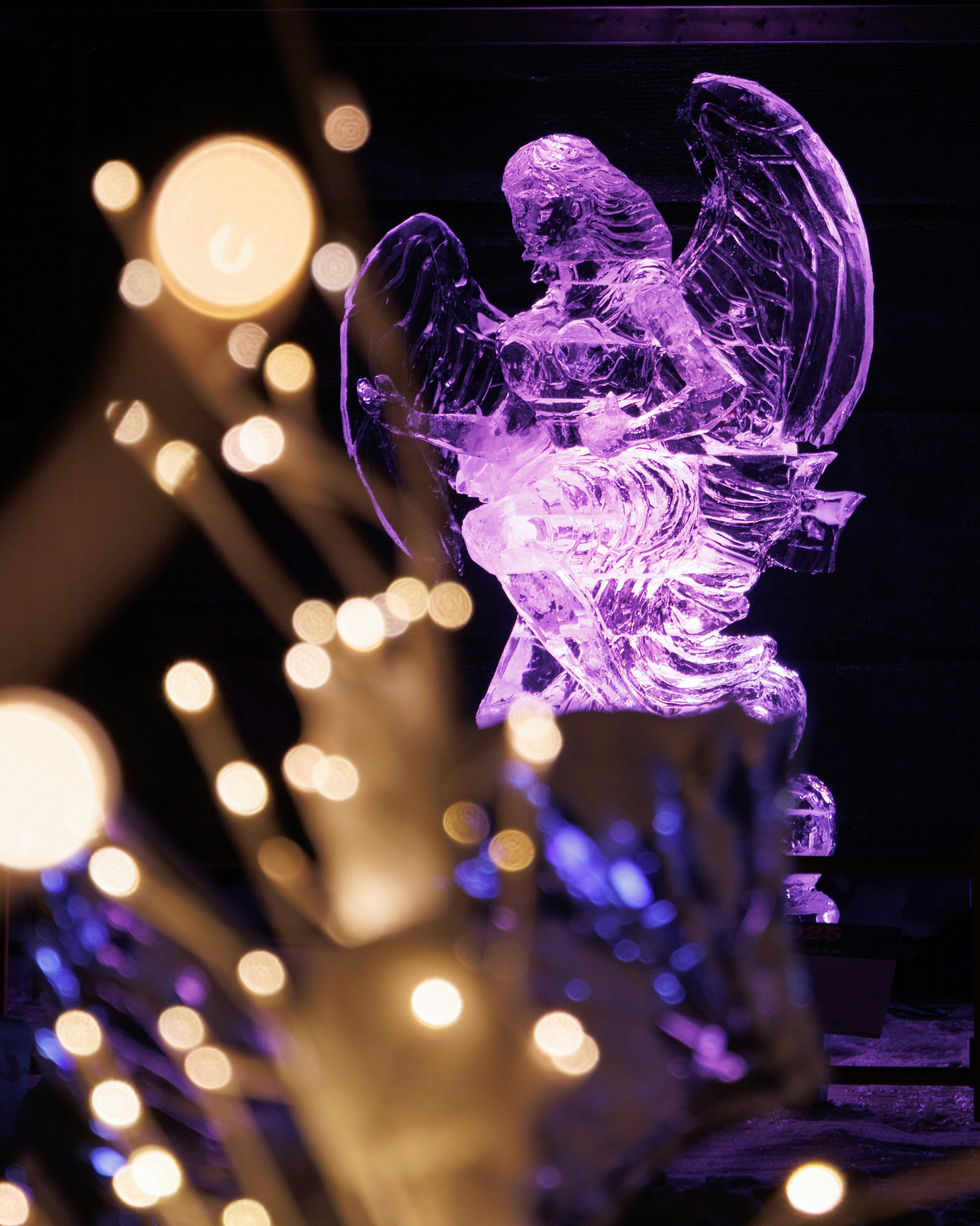 Scultura di ghiaccio a forma di angelo illuminata da luci viola con luci sfocate in primo piano