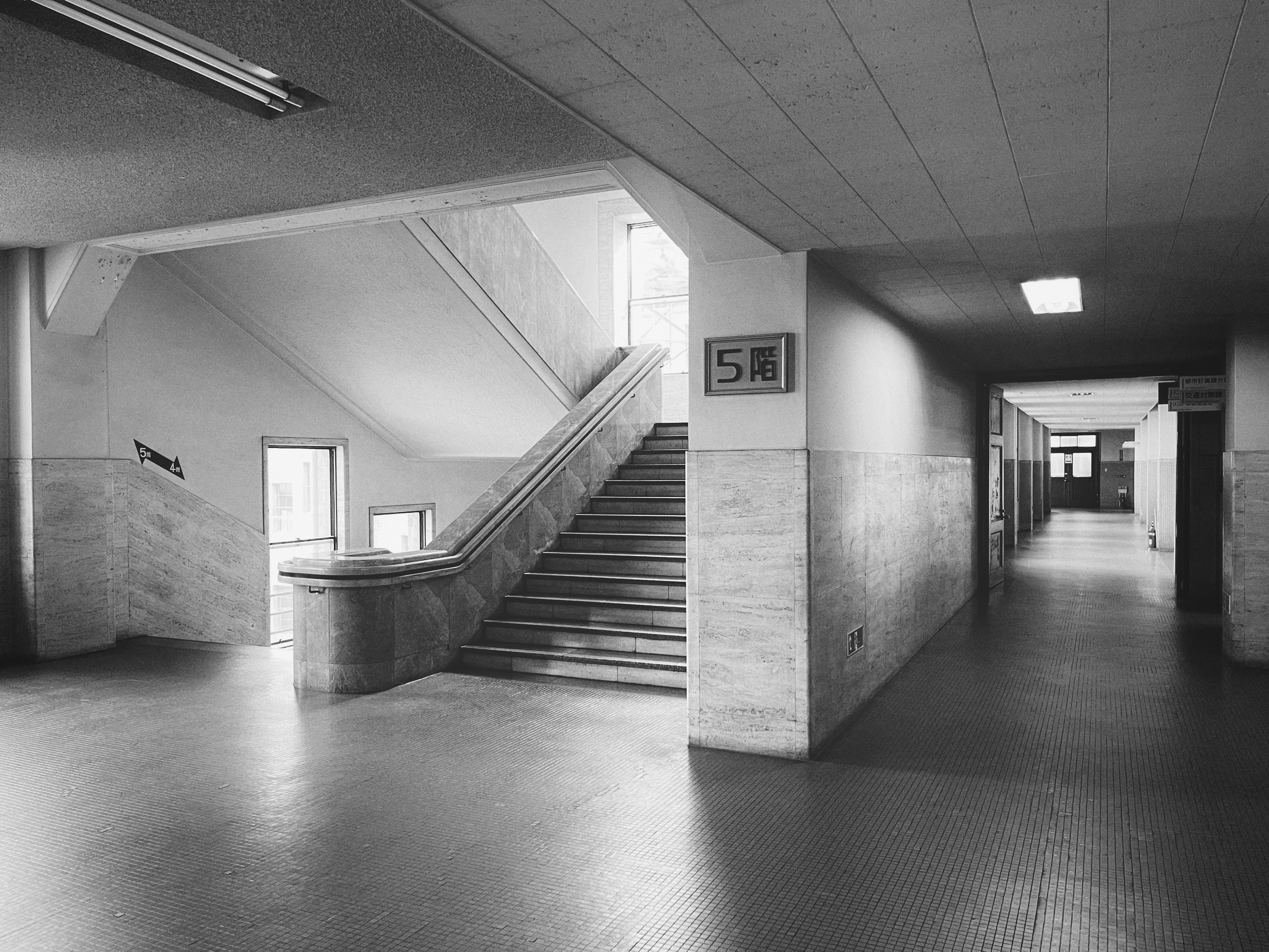 Interno di una scuola in bianco e nero con scale e un lungo corridoio