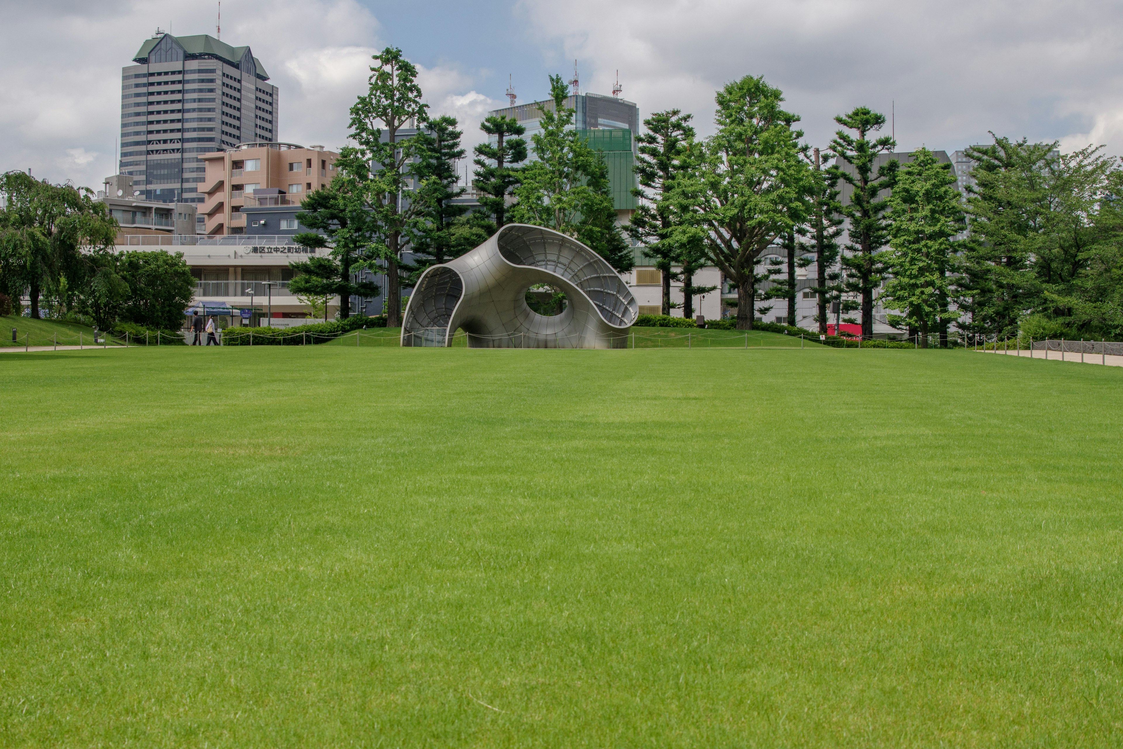 Moderne Skulptur auf grünem Gras mit Wolkenkratzern im Hintergrund