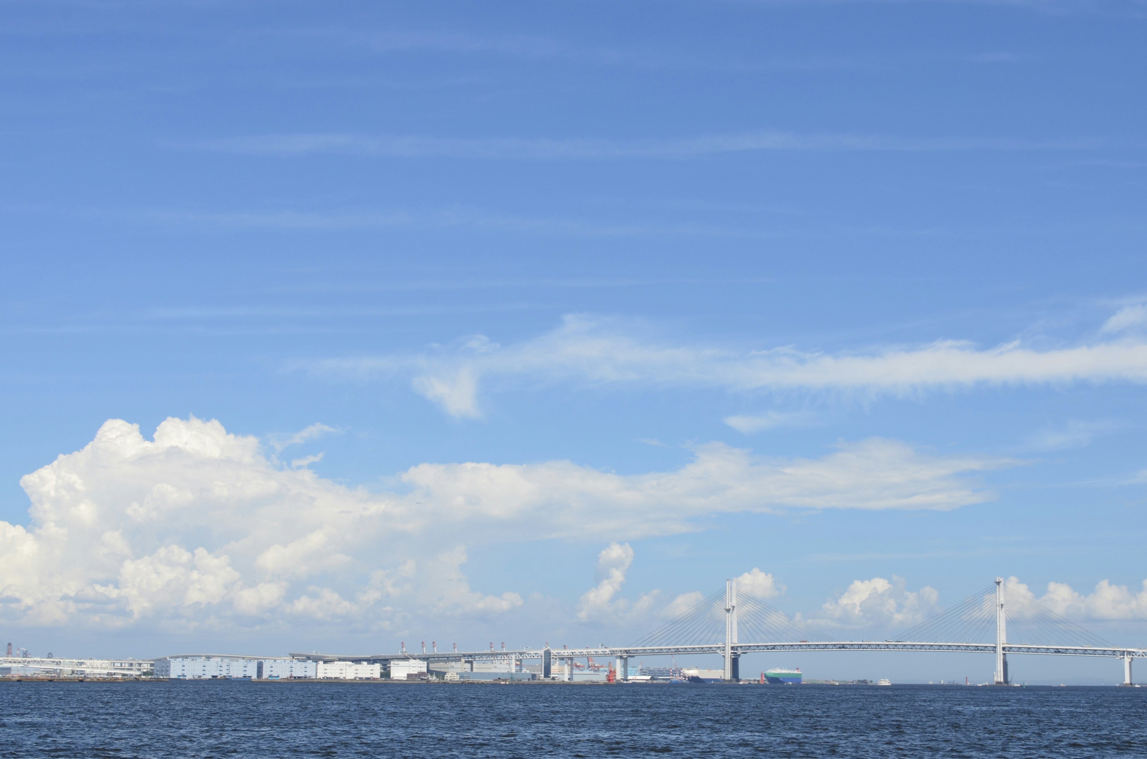 Seascape featuring blue sky white clouds and a bridge in the distance