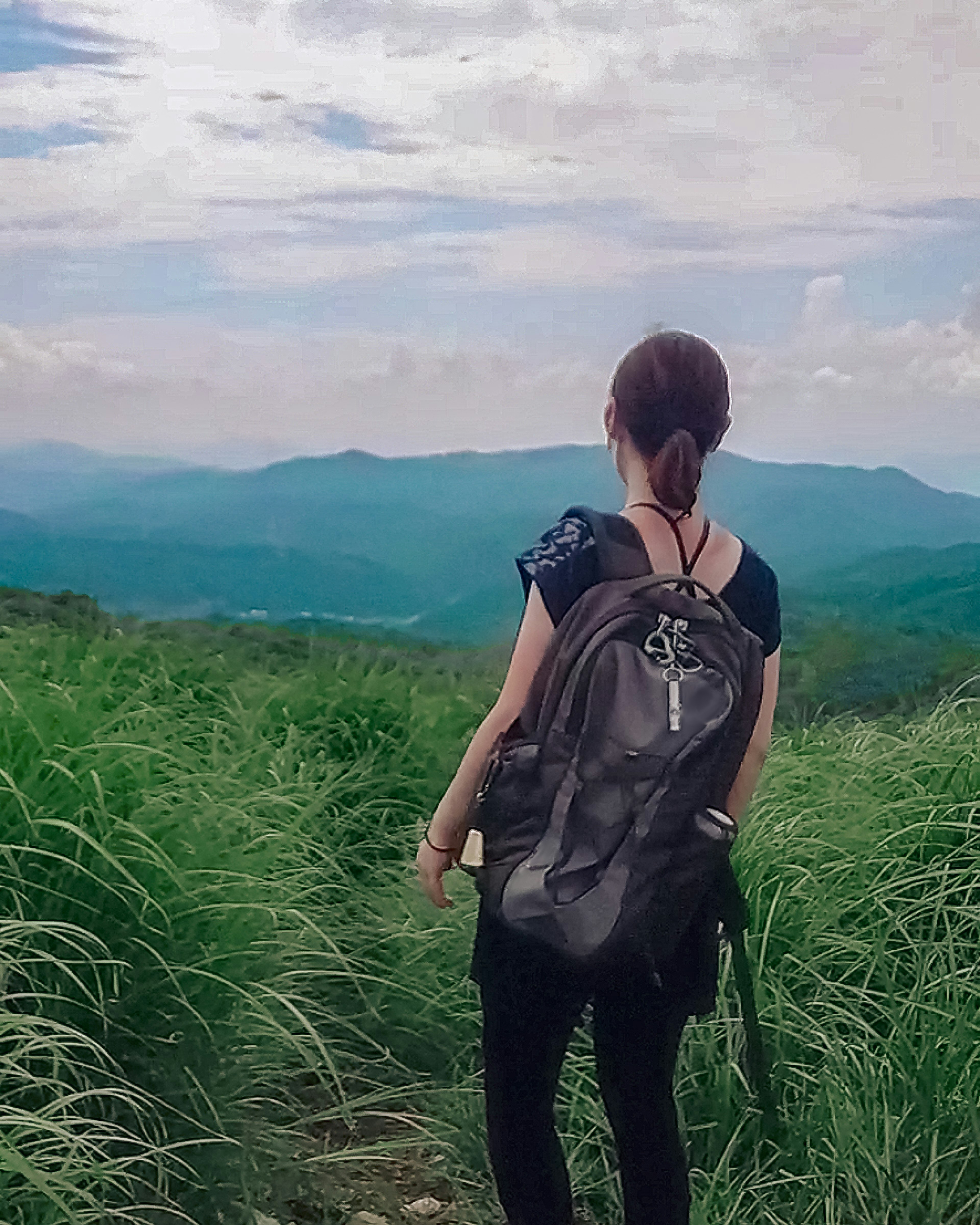 Wanita berdiri di ladang hijau menghadap gunung