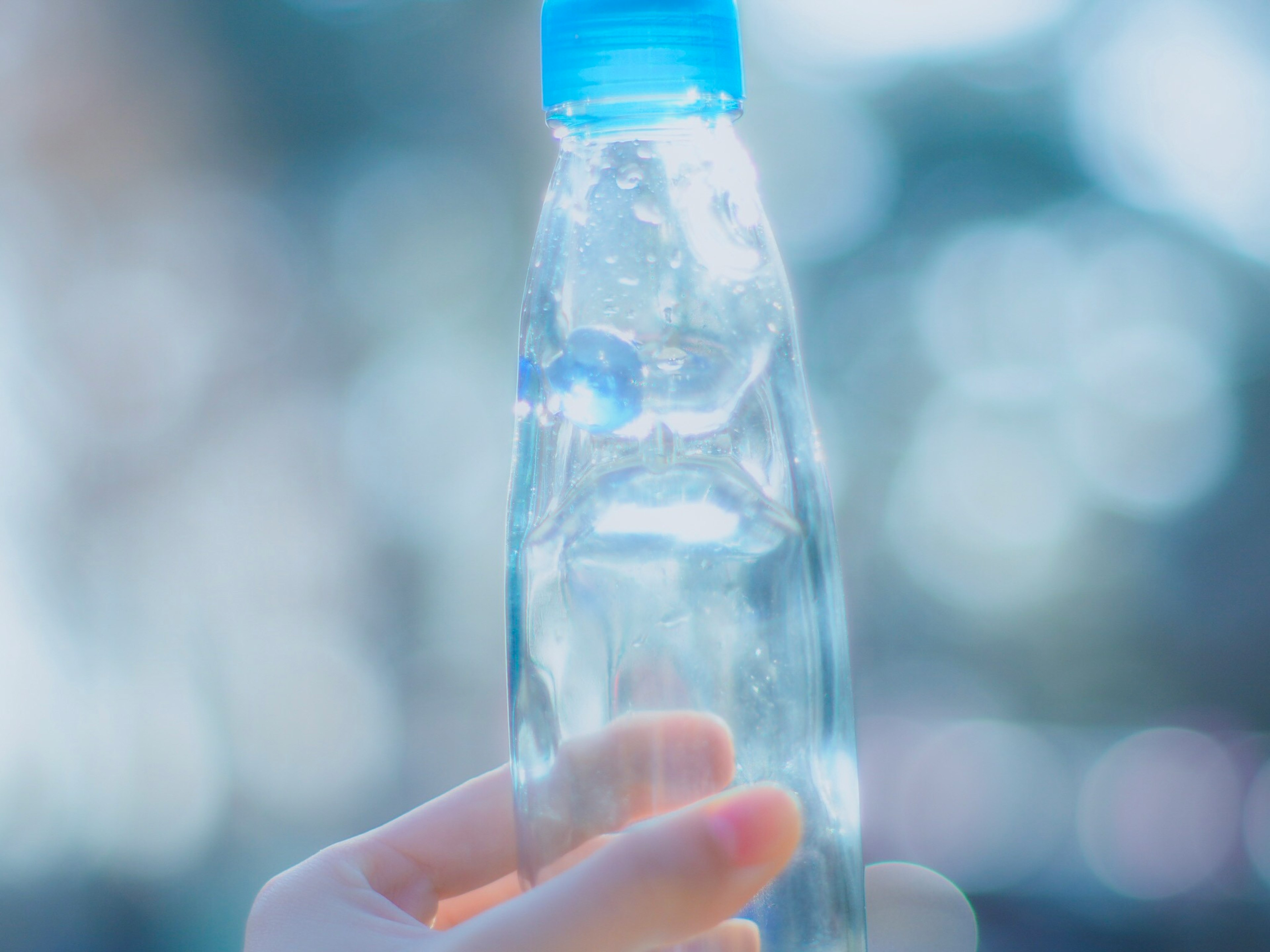 Primo piano di una mano che tiene una bottiglia d'acqua trasparente