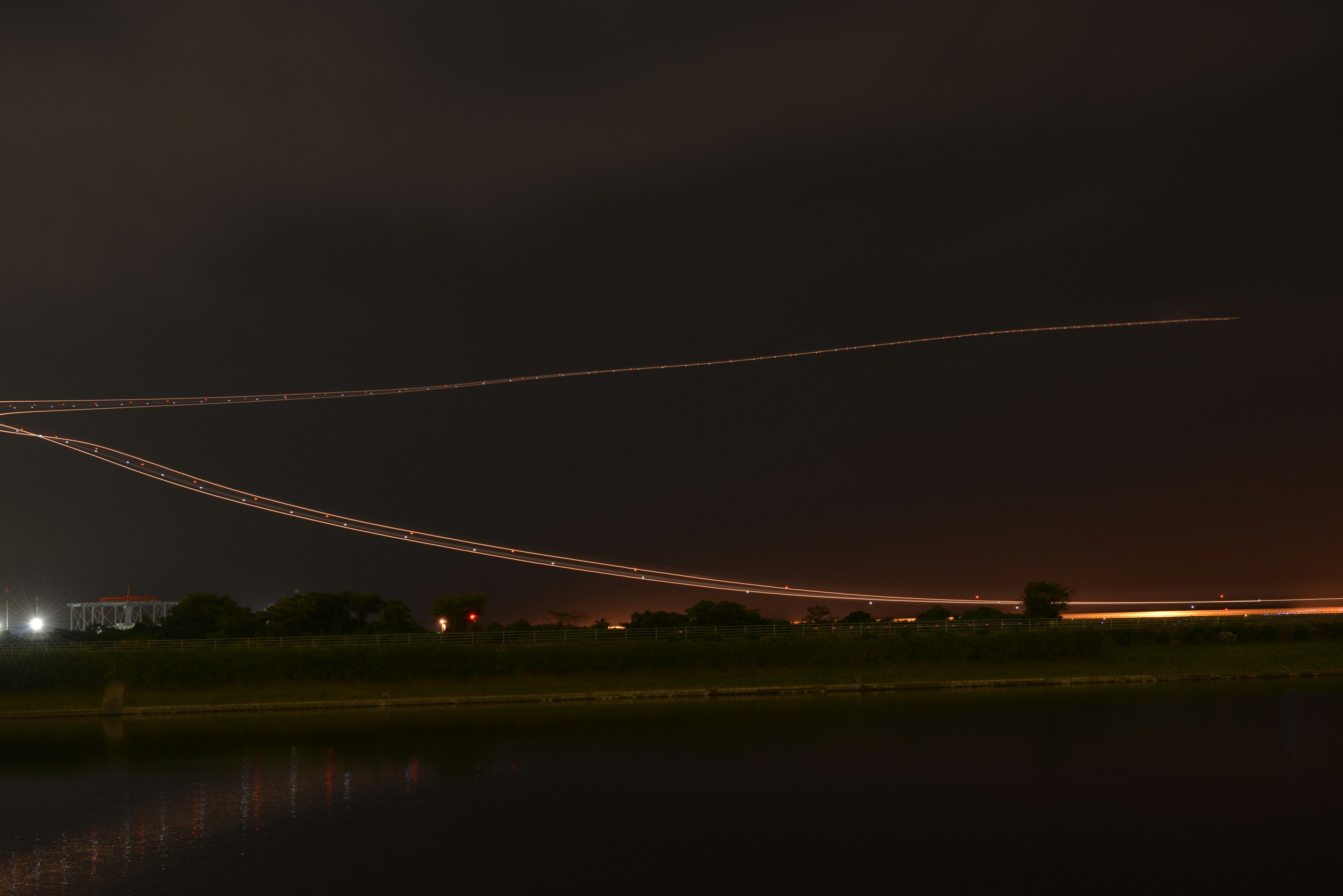 Ciel nocturne avec des traînées lumineuses d'avion se reflétant sur l'eau lumières de la ville et nuages