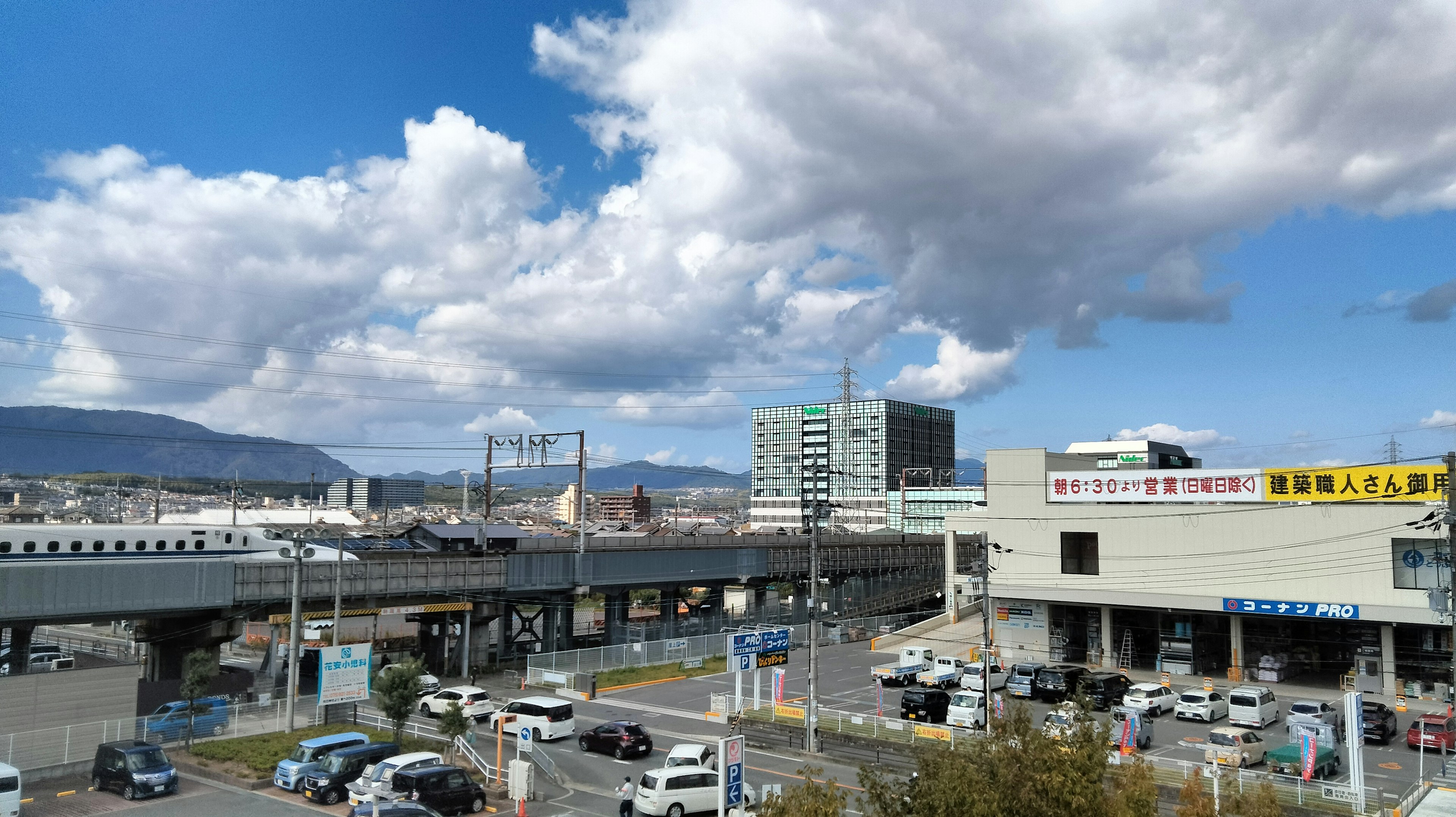 Un paisaje urbano con cielo azul y nubes esponjosas con trenes y vehículos en movimiento