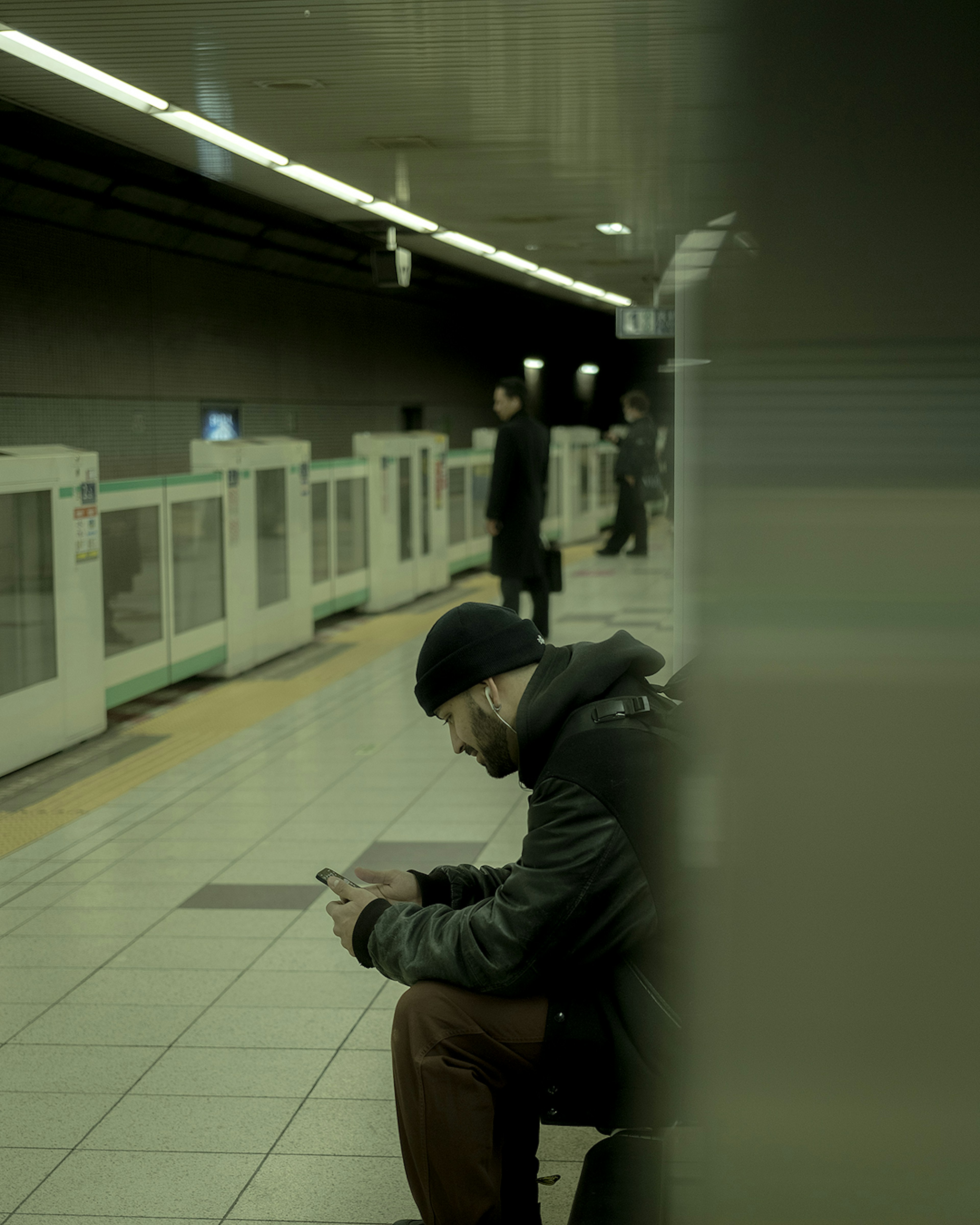 Mann, der ein Smartphone an einer U-Bahn-Station mit anderen Fahrgästen benutzt