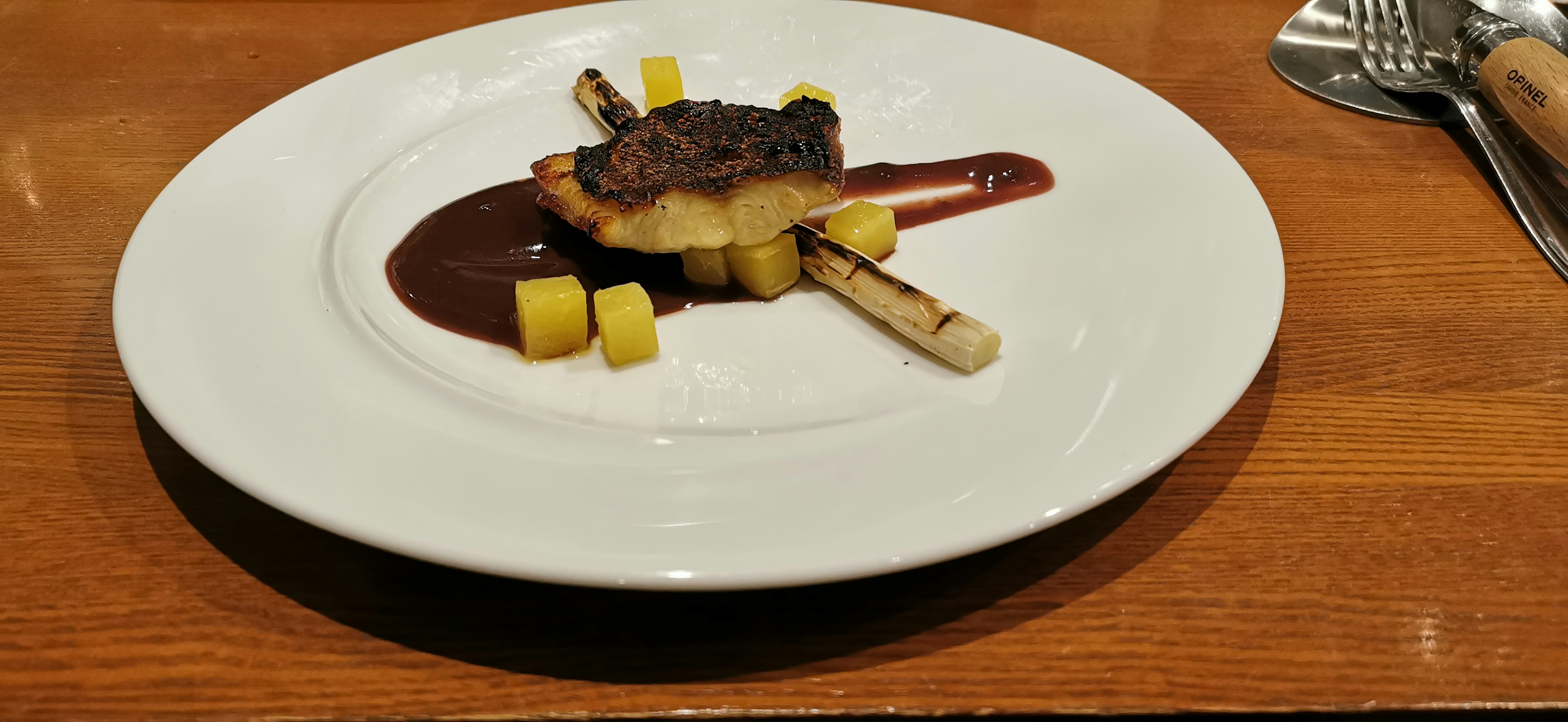 Grilled dish served on a white plate with sweet sauce and fruit cubes