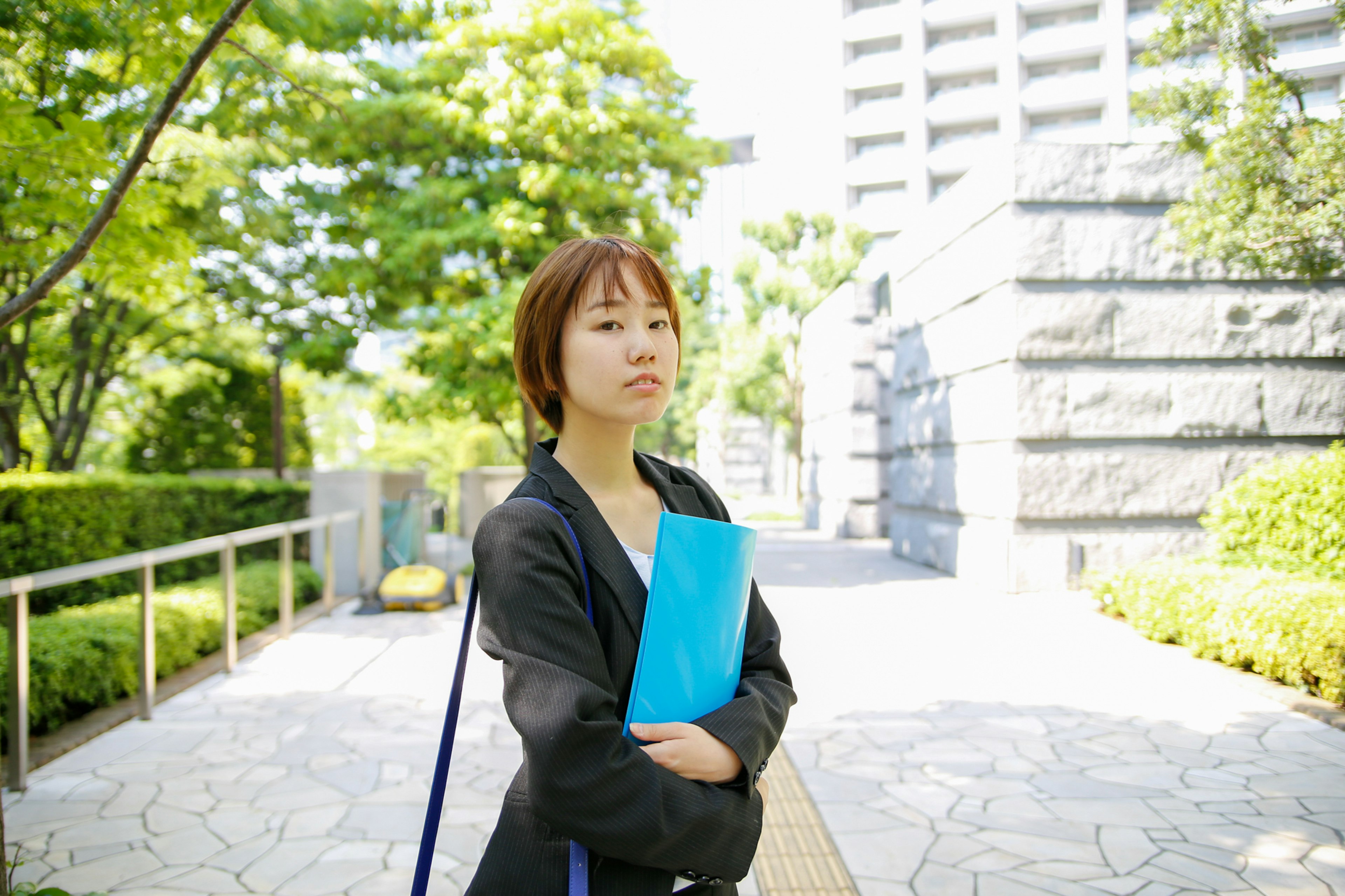 Eine Frau in Businesskleidung, die eine blaue Mappe in einem Park hält