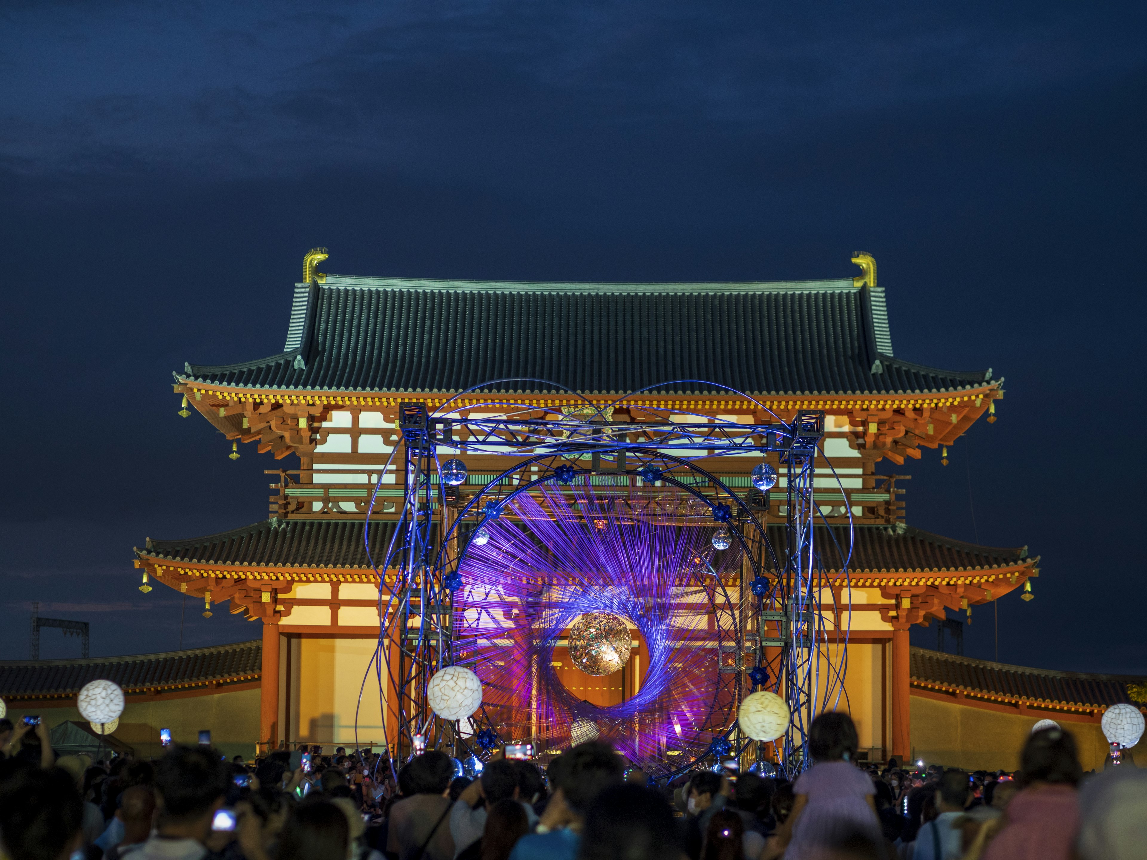 Escena de festival con un edificio tradicional y un escenario moderno iluminado por la noche