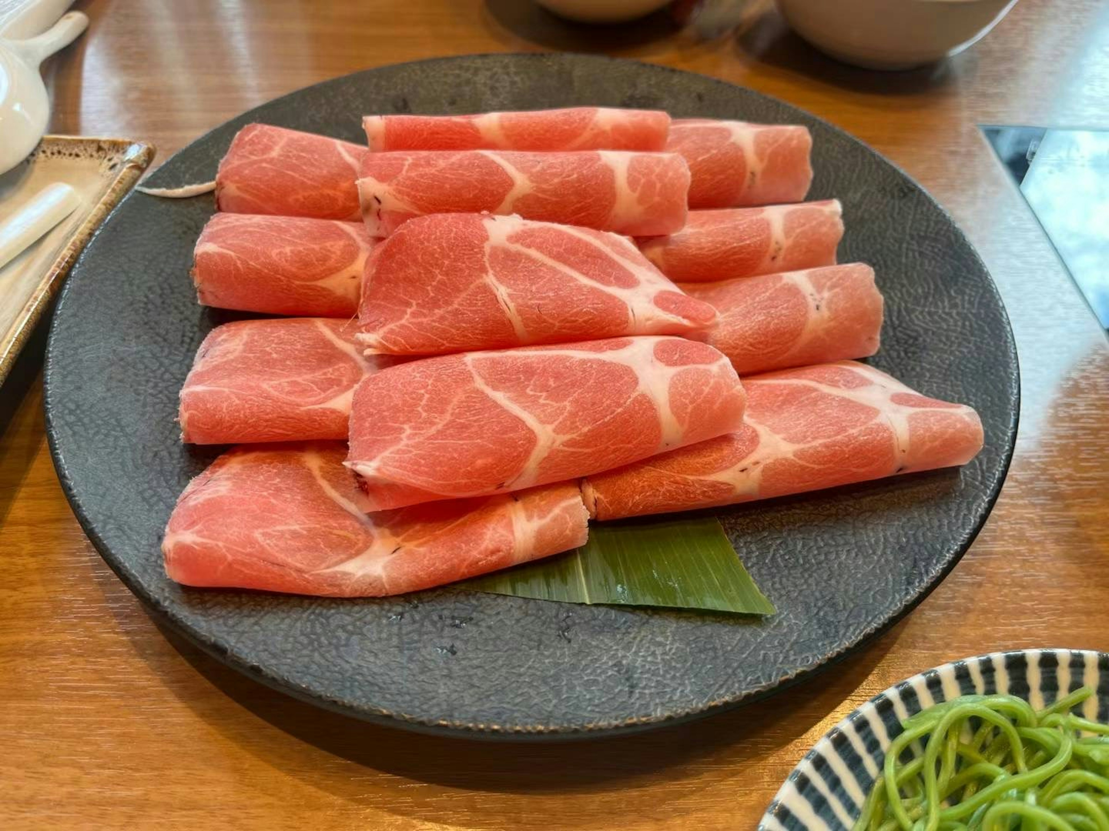 Thin slices of pork arranged on a black plate