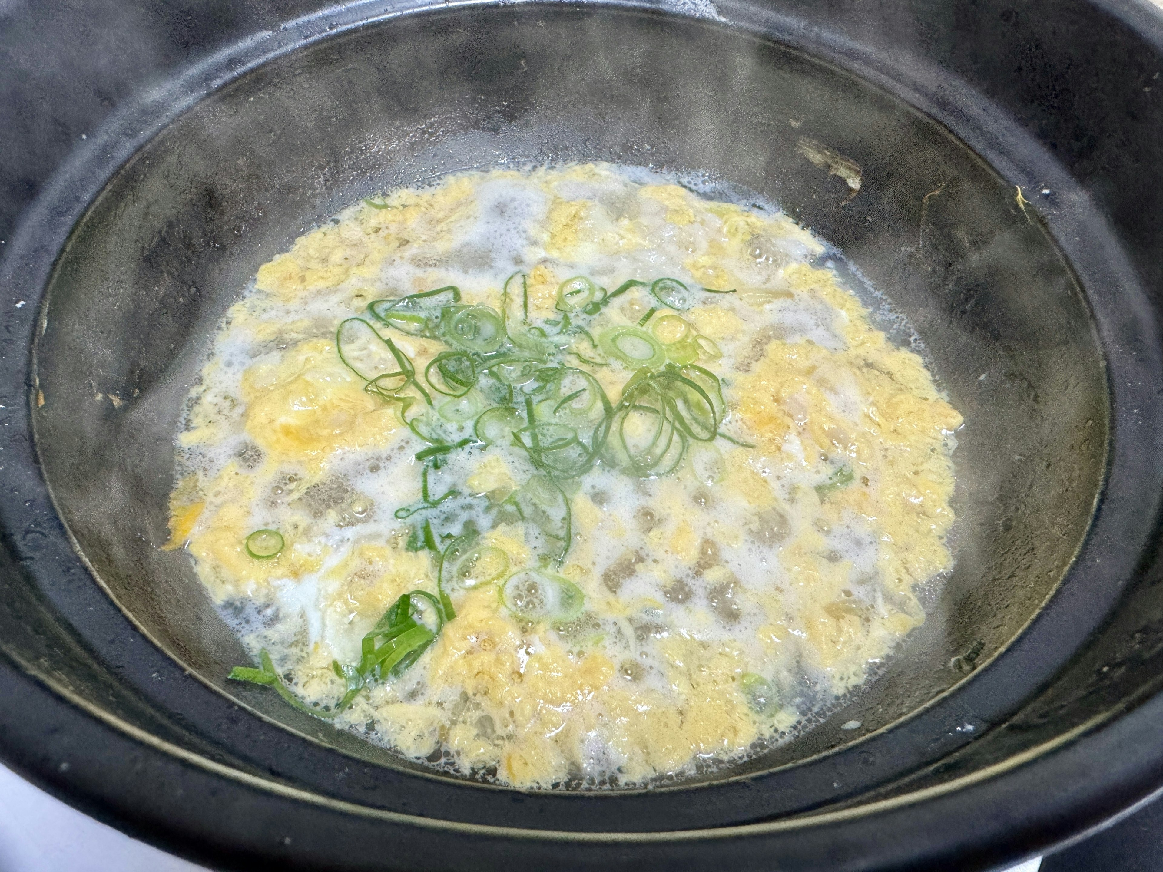 Soupe aux œufs cuisant dans une casserole avec des oignons verts flottants