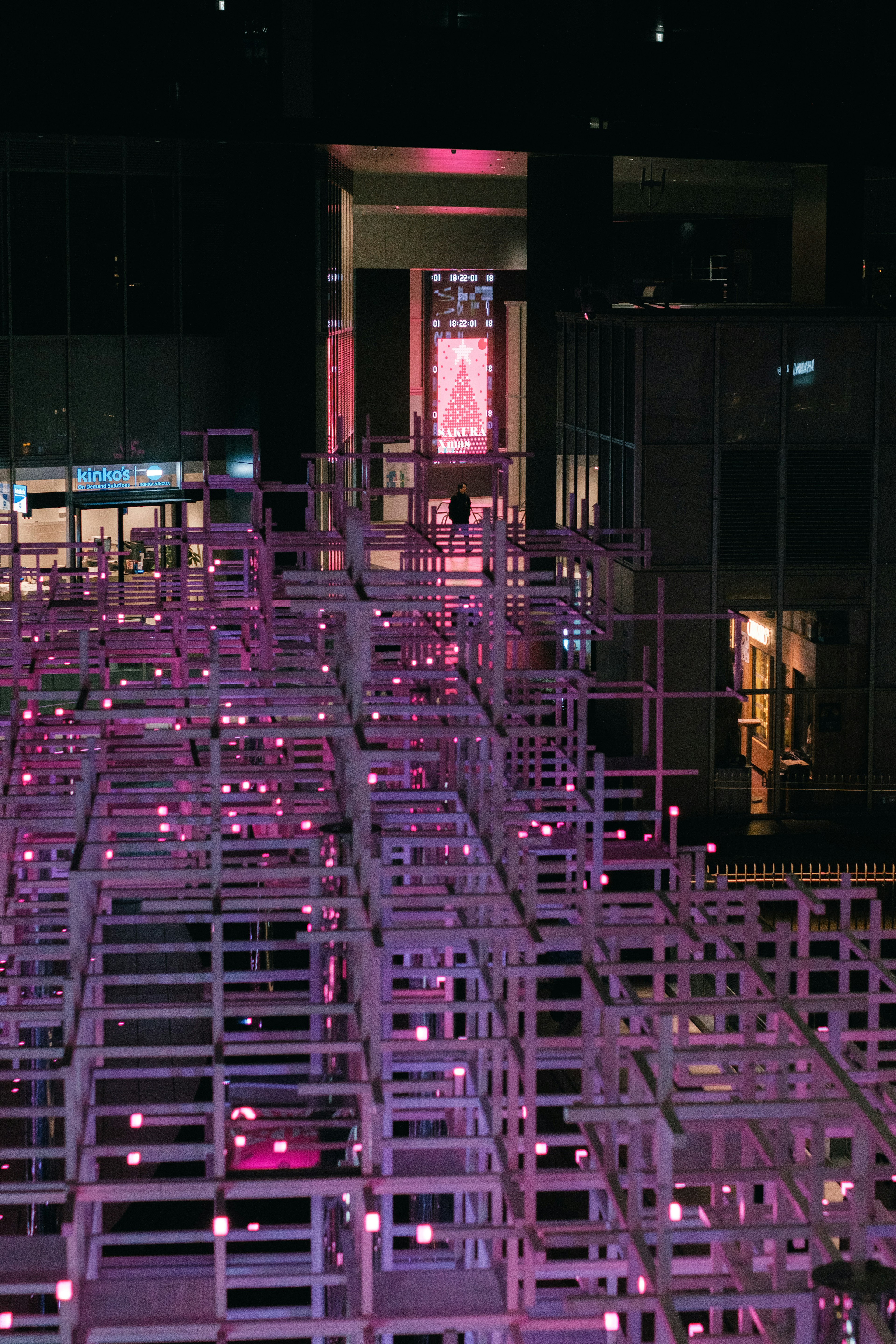 Structure tridimensionnelle illuminée par des lumières roses dans un cadre urbain nocturne