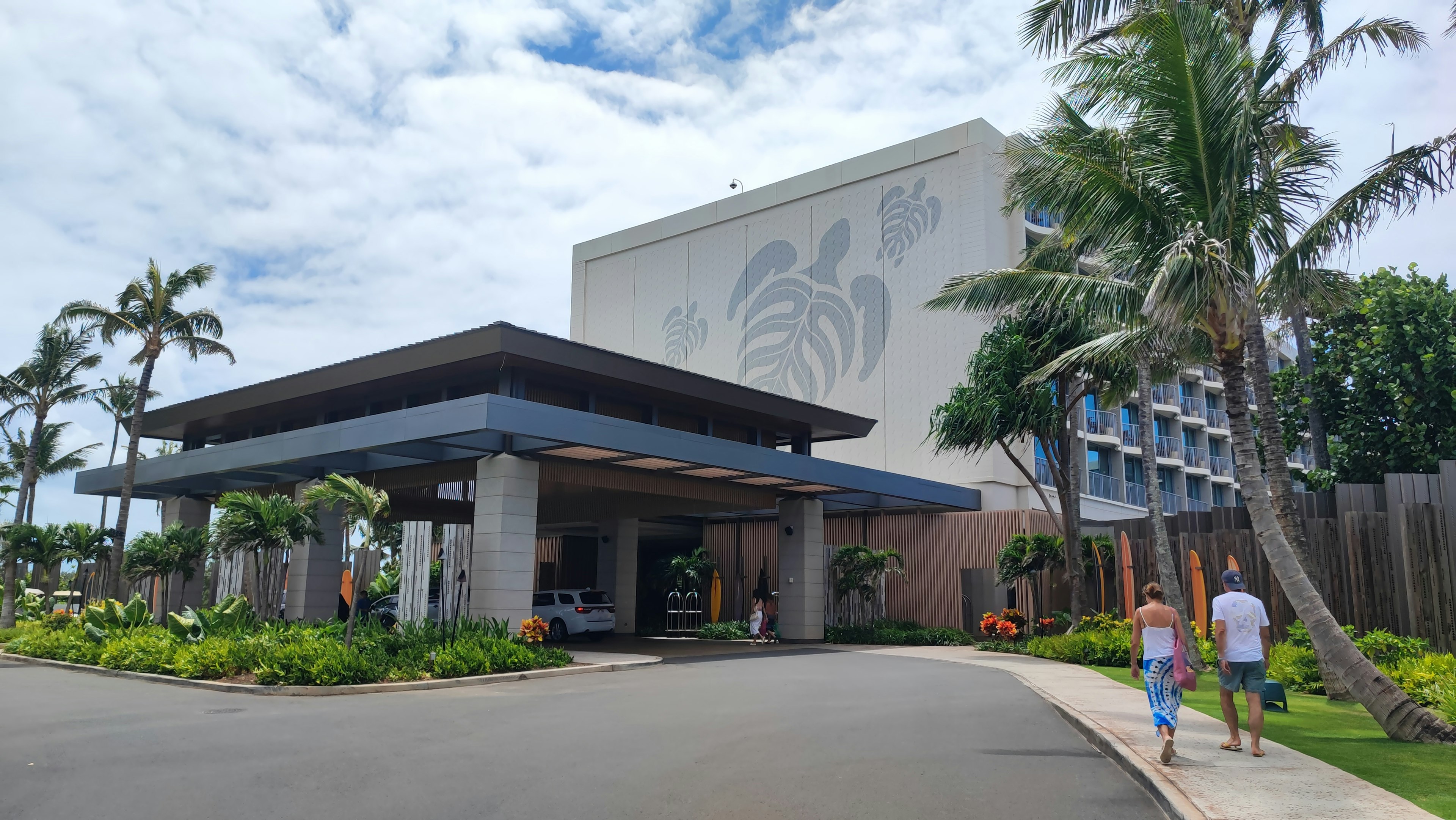 Entrada de un hotel resort con plantas tropicales y cielo nublado