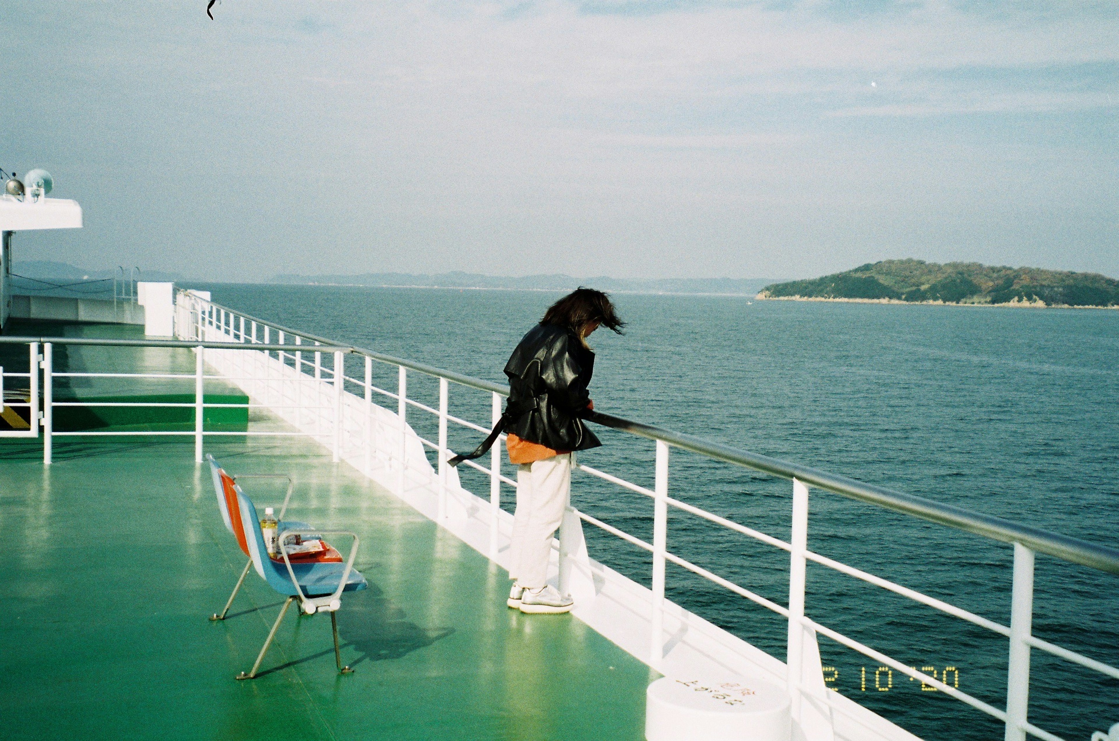 Persona de pie en la cubierta de un ferry mirando al océano con una silla cercana