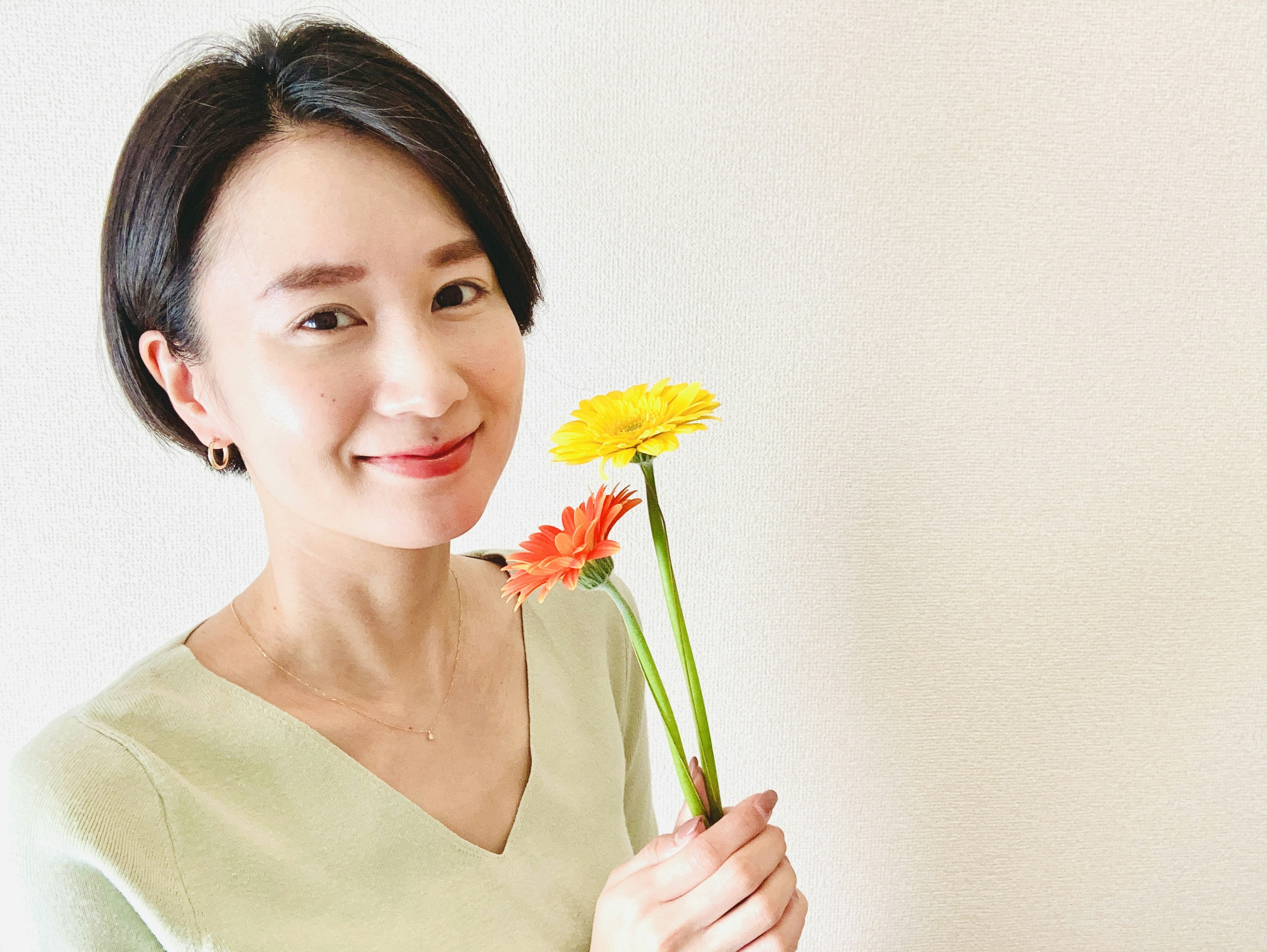 Woman smiling while holding yellow and orange flowers against a simple background