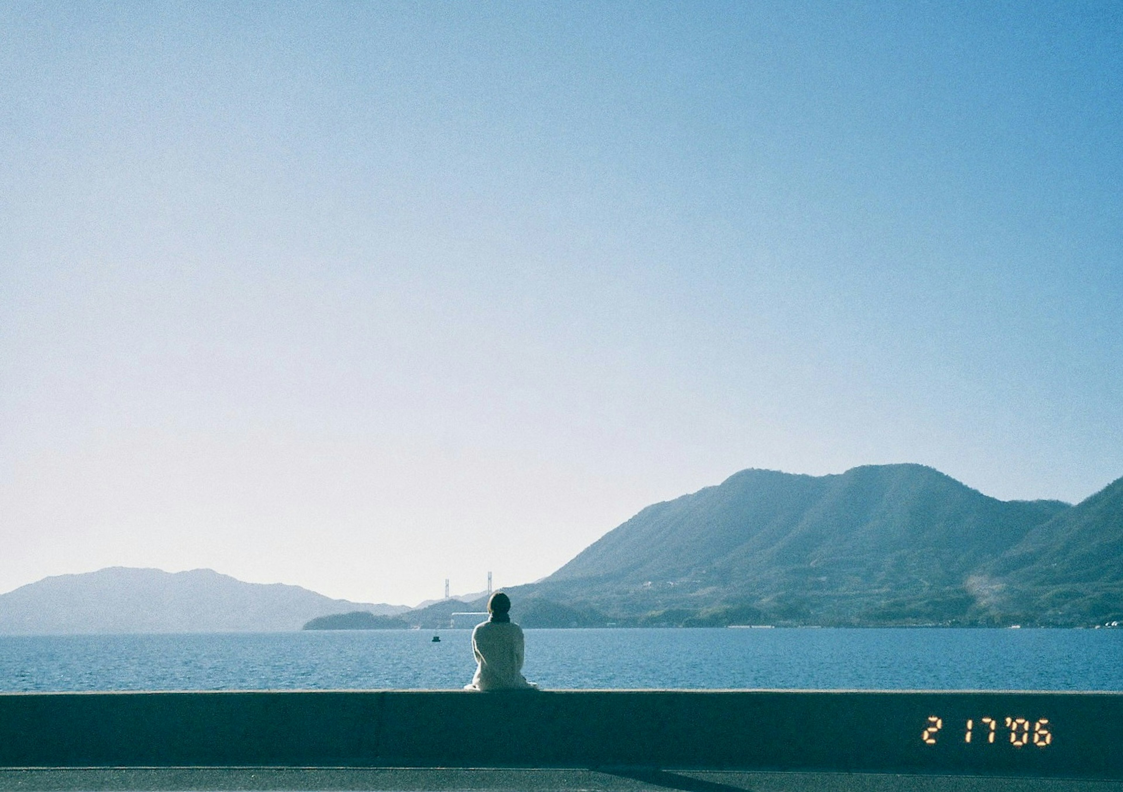 Person gazing at the sea with mountains in the background