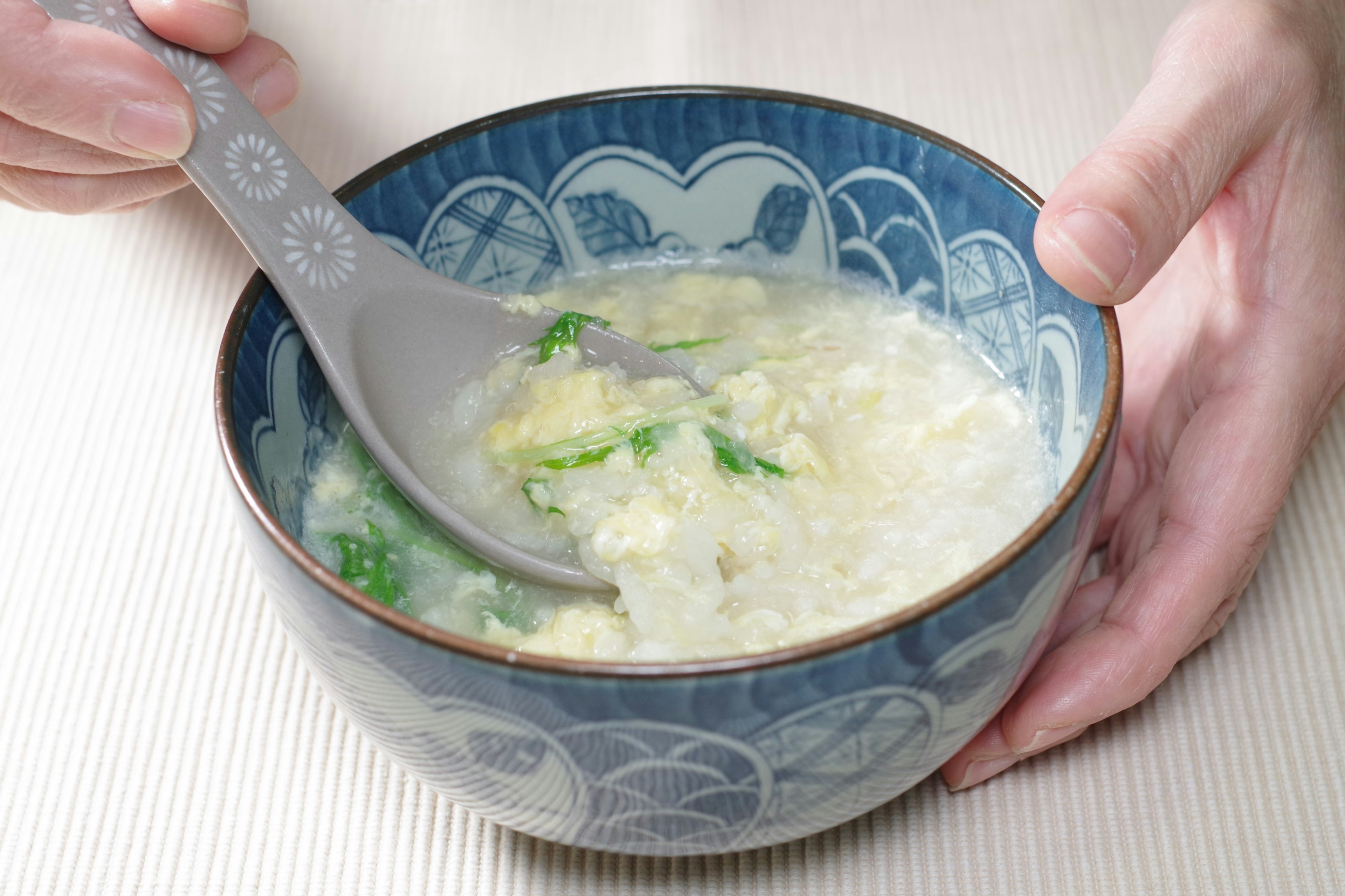 A hand holding a spoon in a blue bowl of soup