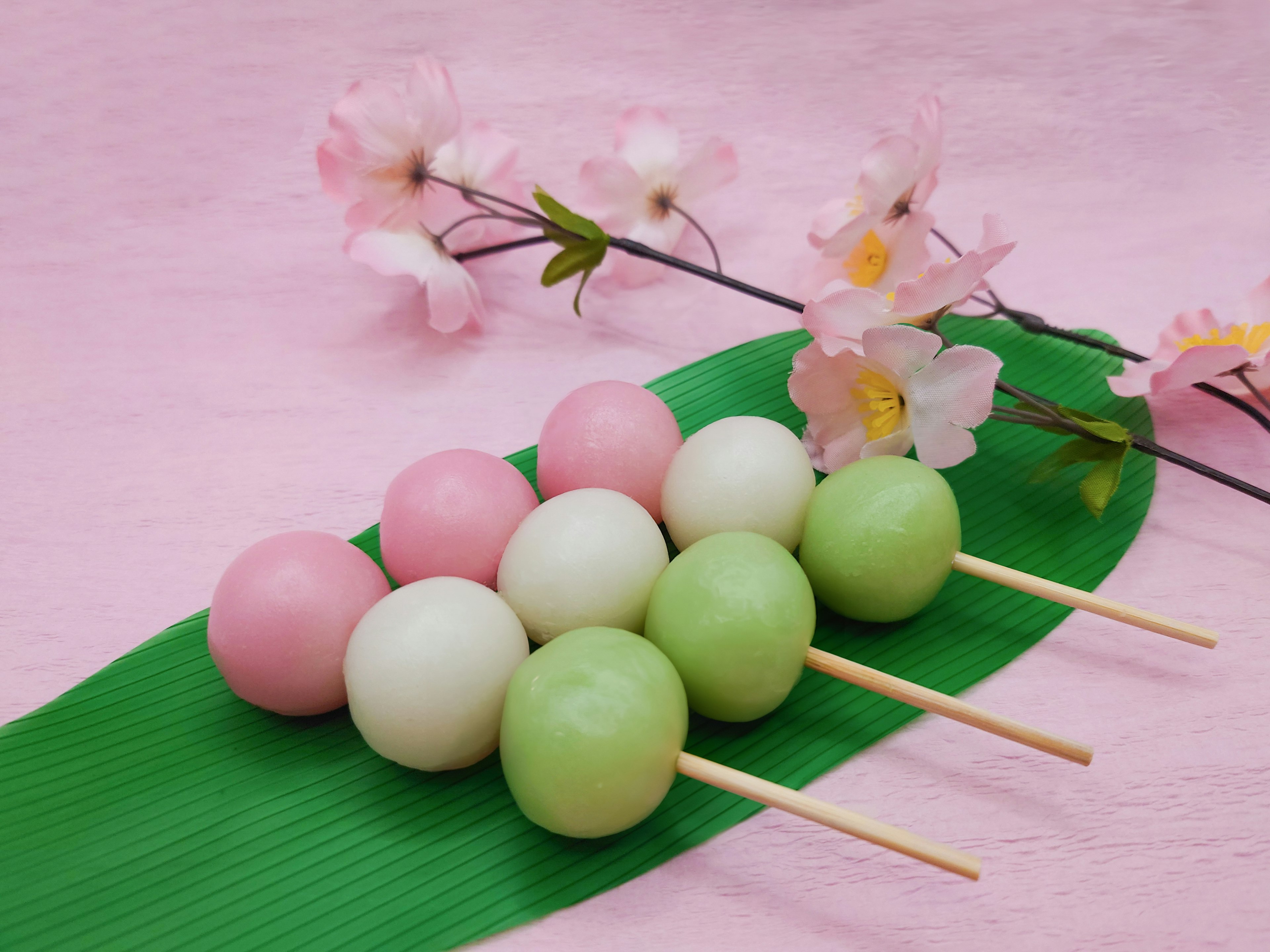 Tusuk sate dango berwarna-warni dengan bunga sakura di latar belakang