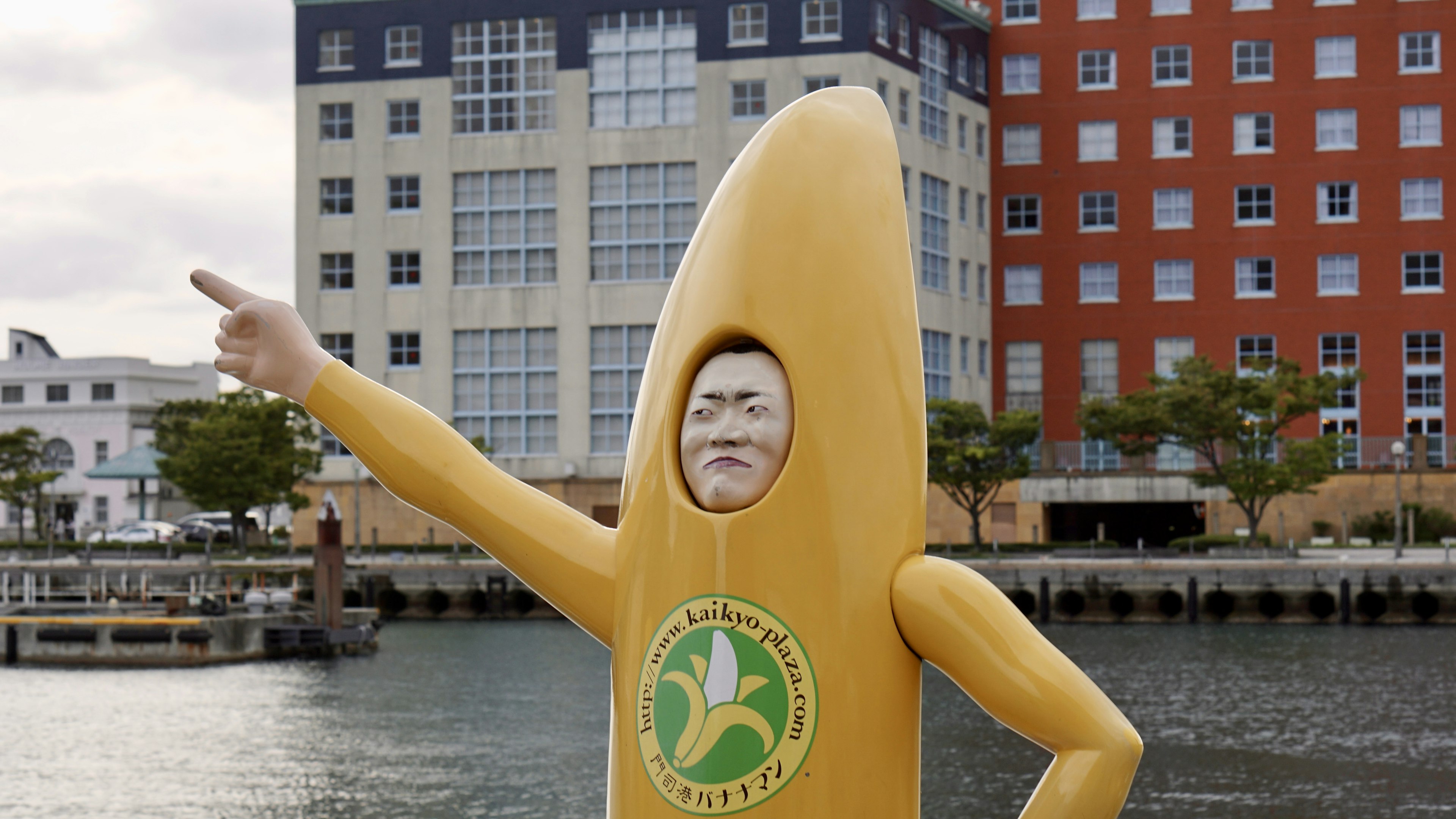 A yellow character statue pointing with a facial expression at a harbor backdrop