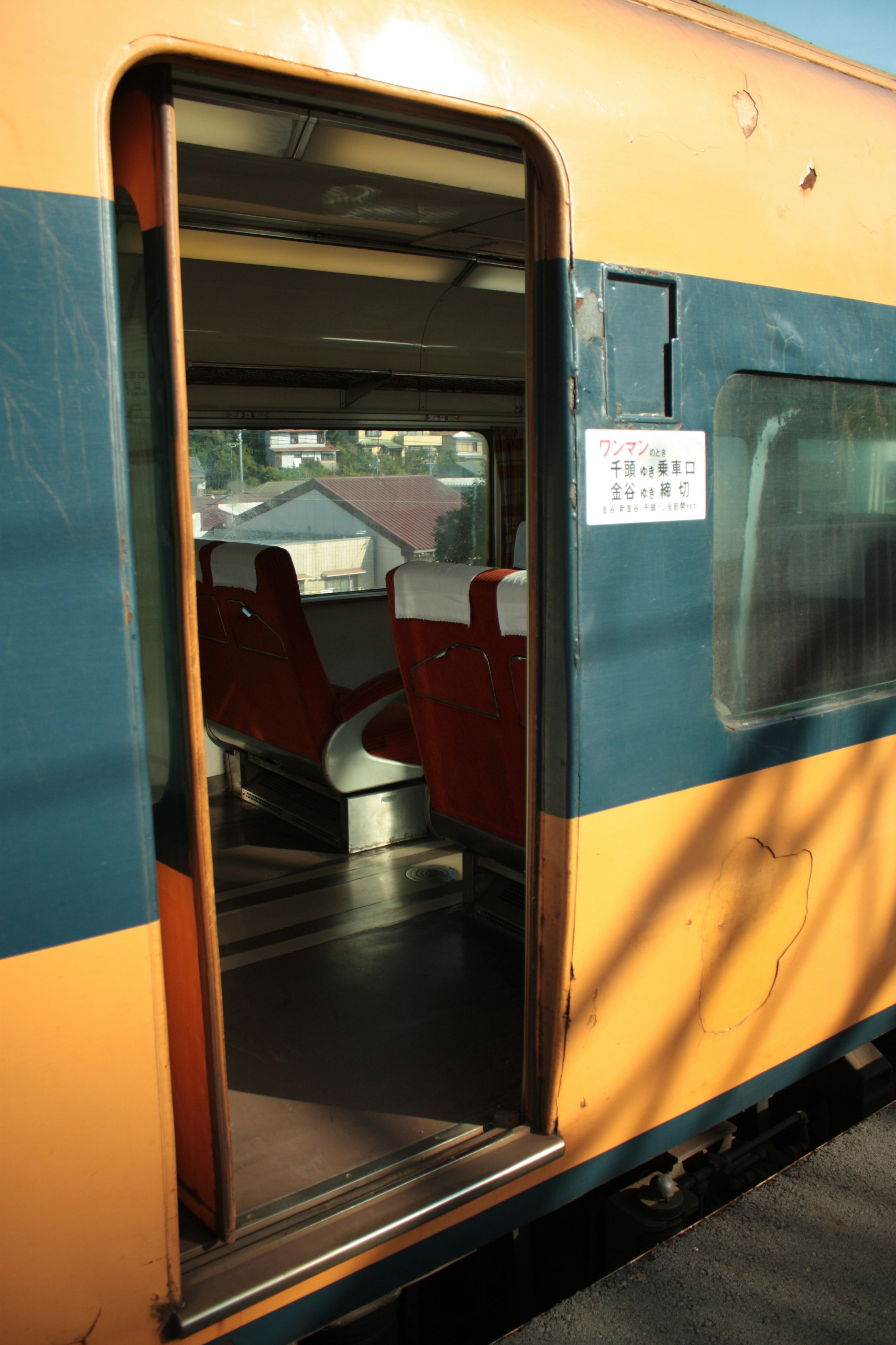 Porte ouverte d'un train orange et bleu révélant l'intérieur avec des sièges rouges