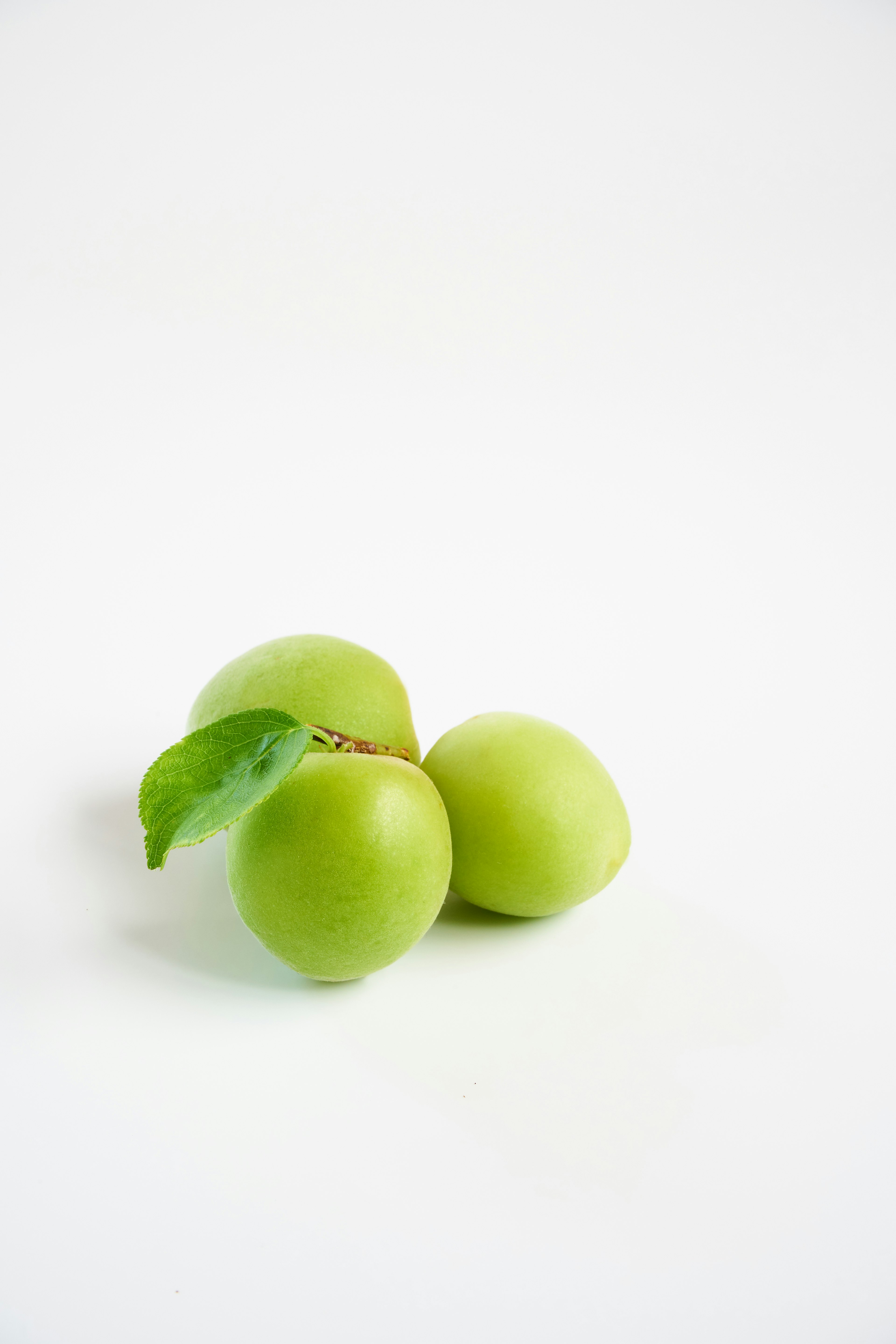 Tres frutas verdes con una hoja en un fondo blanco