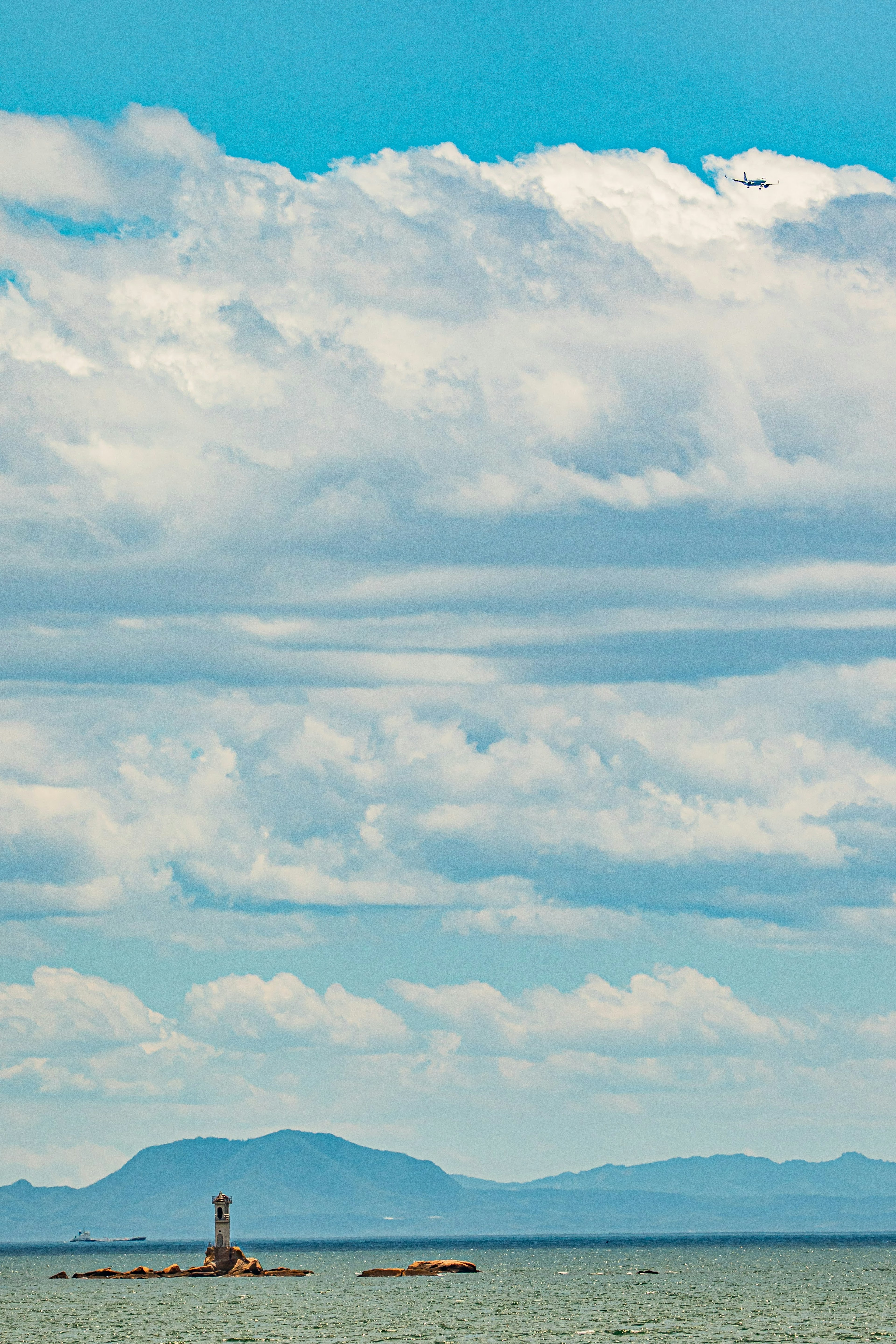 A small lighthouse stands against a backdrop of blue sea and clouds