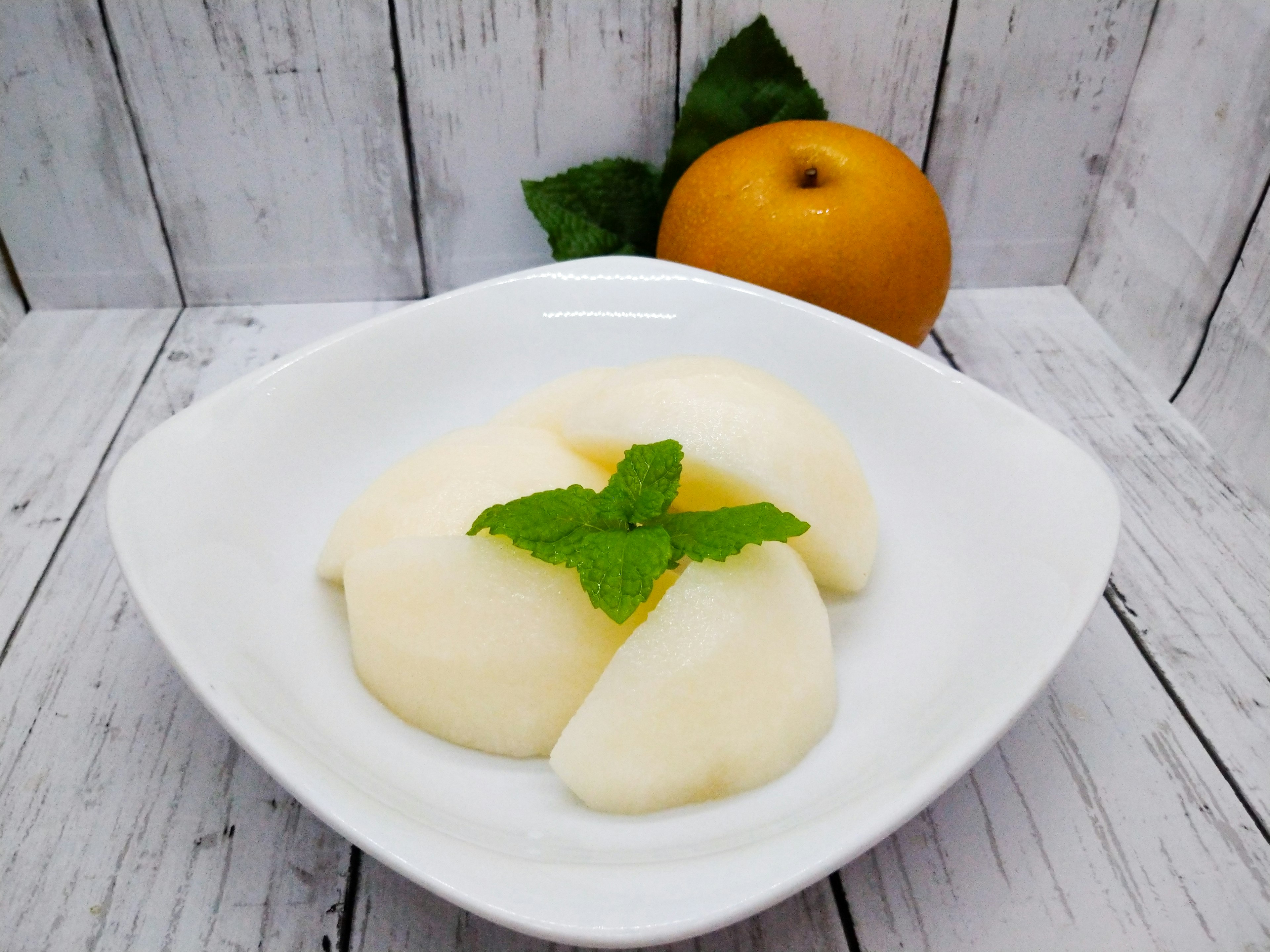 Creamy dessert served on a white plate with a mint leaf and an orange in the background