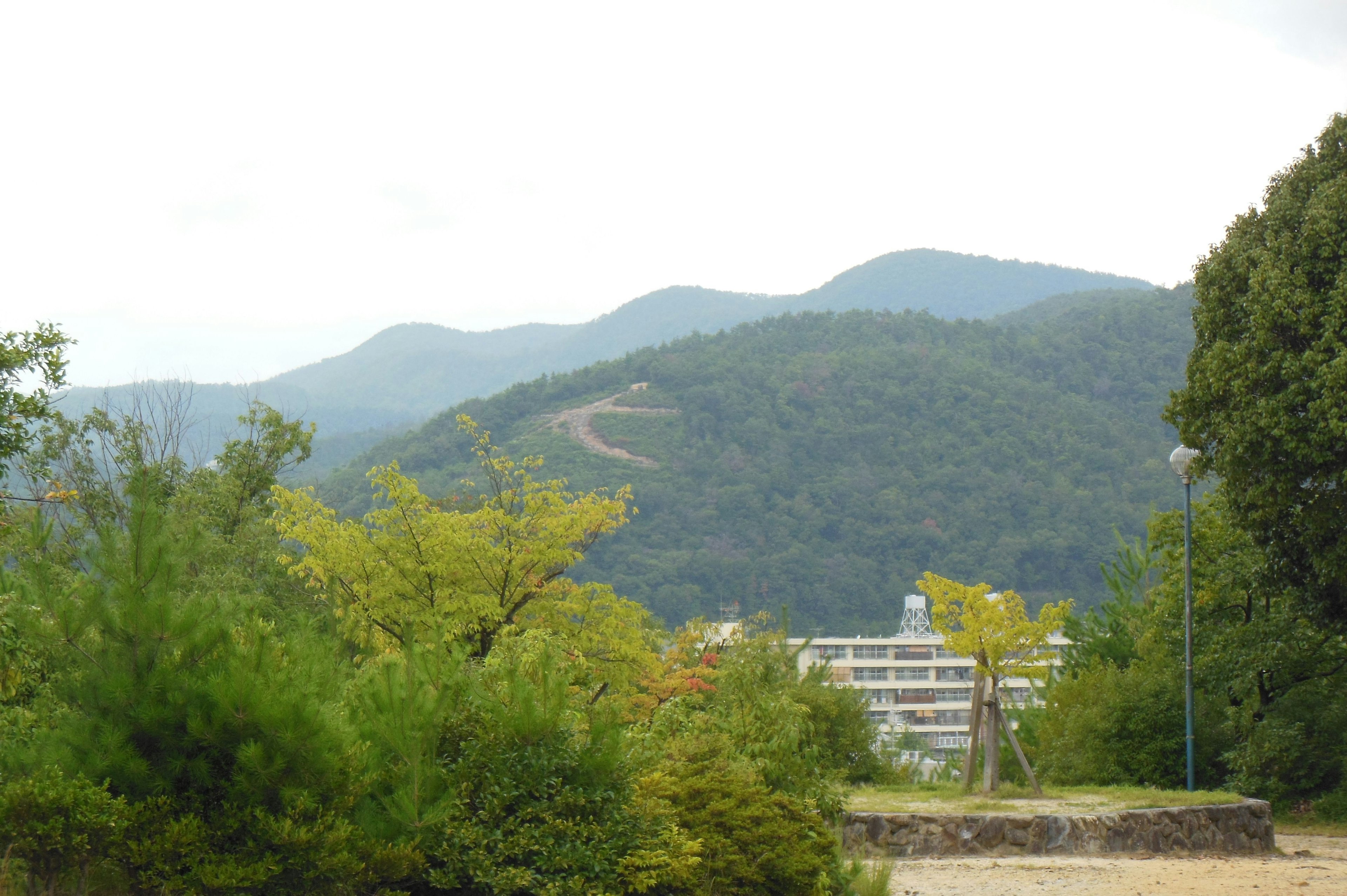 綠色山脈在陰雲下的風景，前景有低矮建築