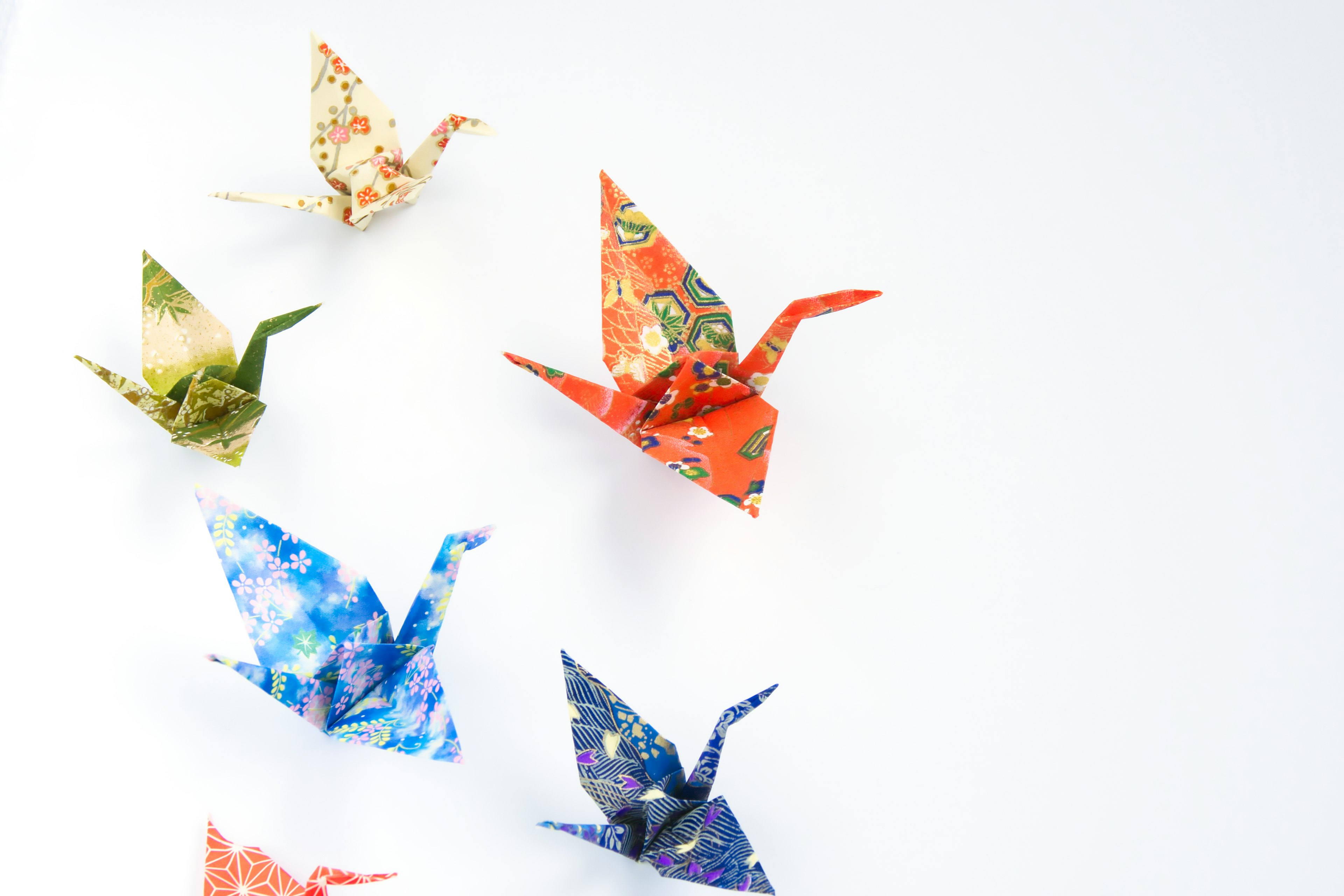 Bunte Origami-Kraniche fliegen vor einem weißen Hintergrund