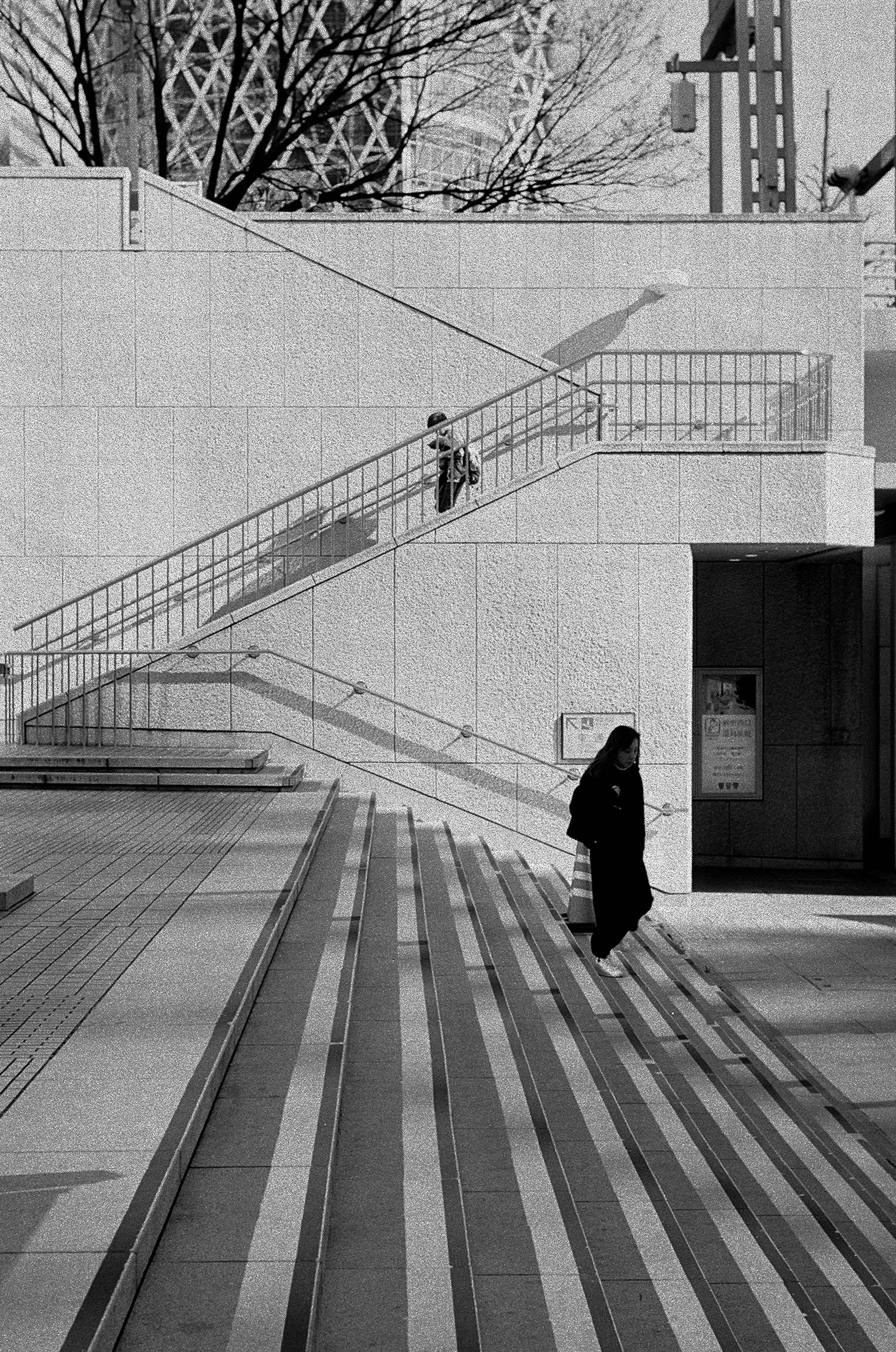 Scène en noir et blanc avec une personne montant des escaliers et une autre descendant