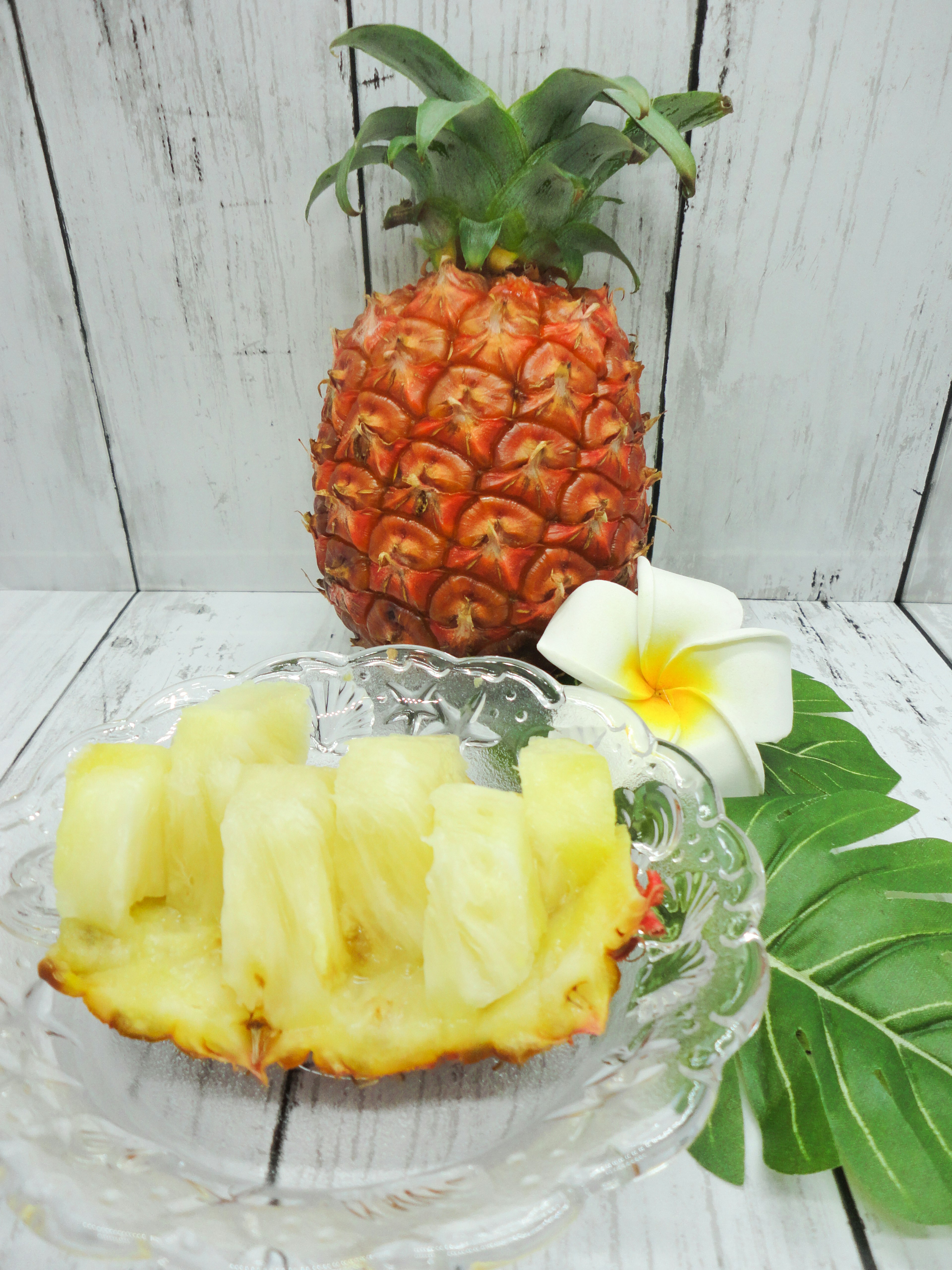 Una piña entera con rodajas en un plato de vidrio decorado con una flor blanca