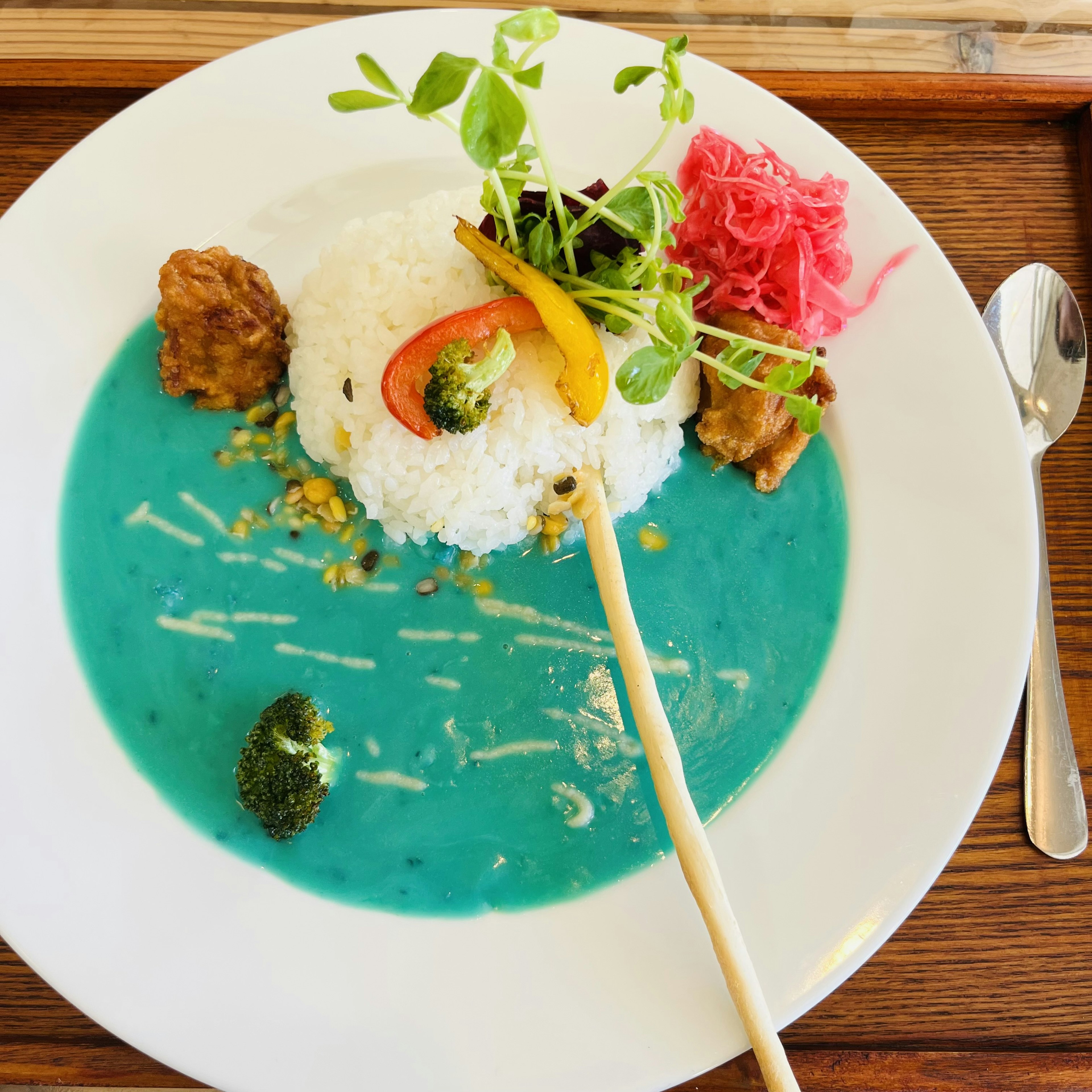 Colorful dish featuring rice surrounded by bright blue soup and various vegetables