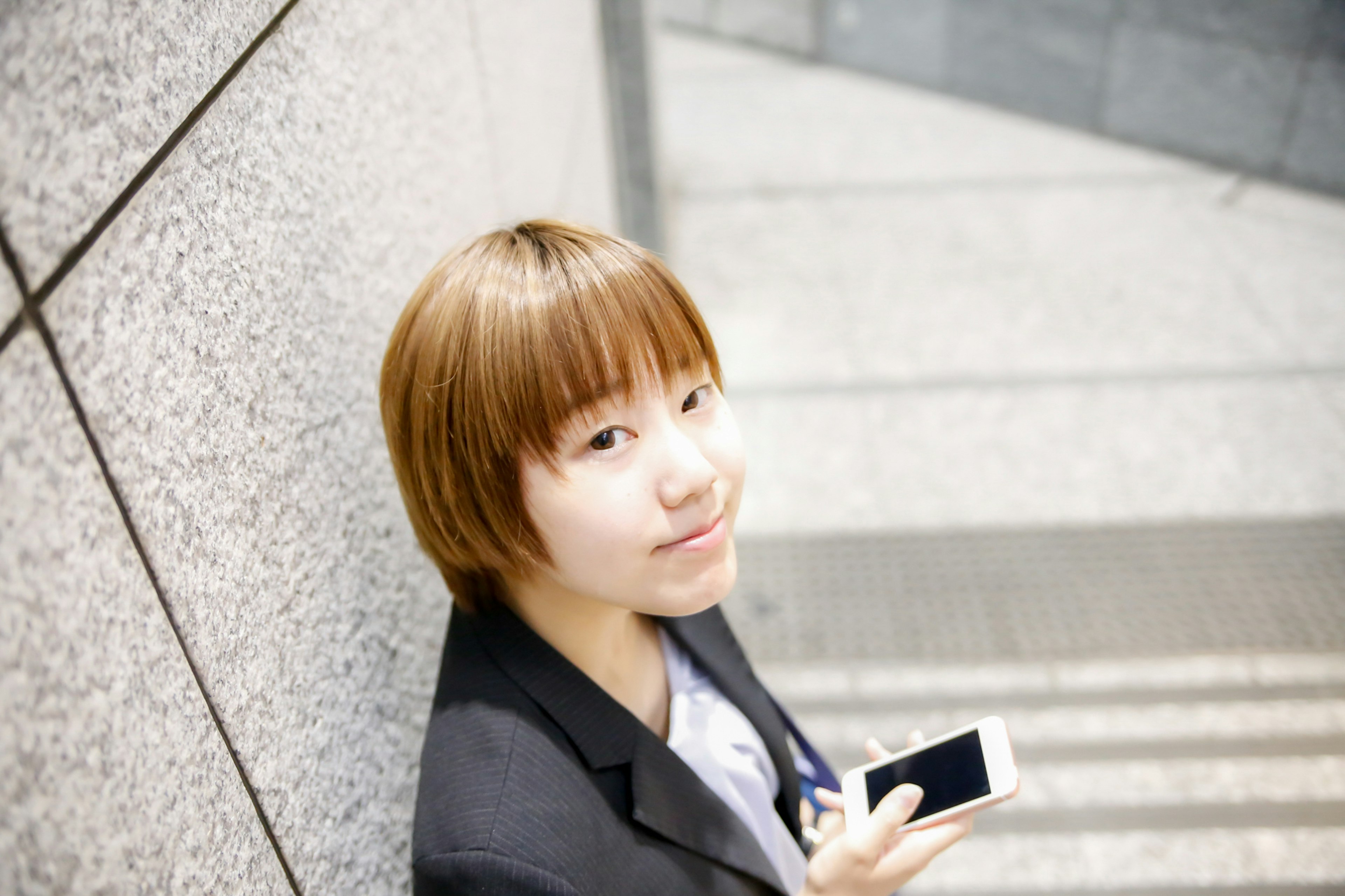 Young woman smiling while holding a smartphone against a gray background