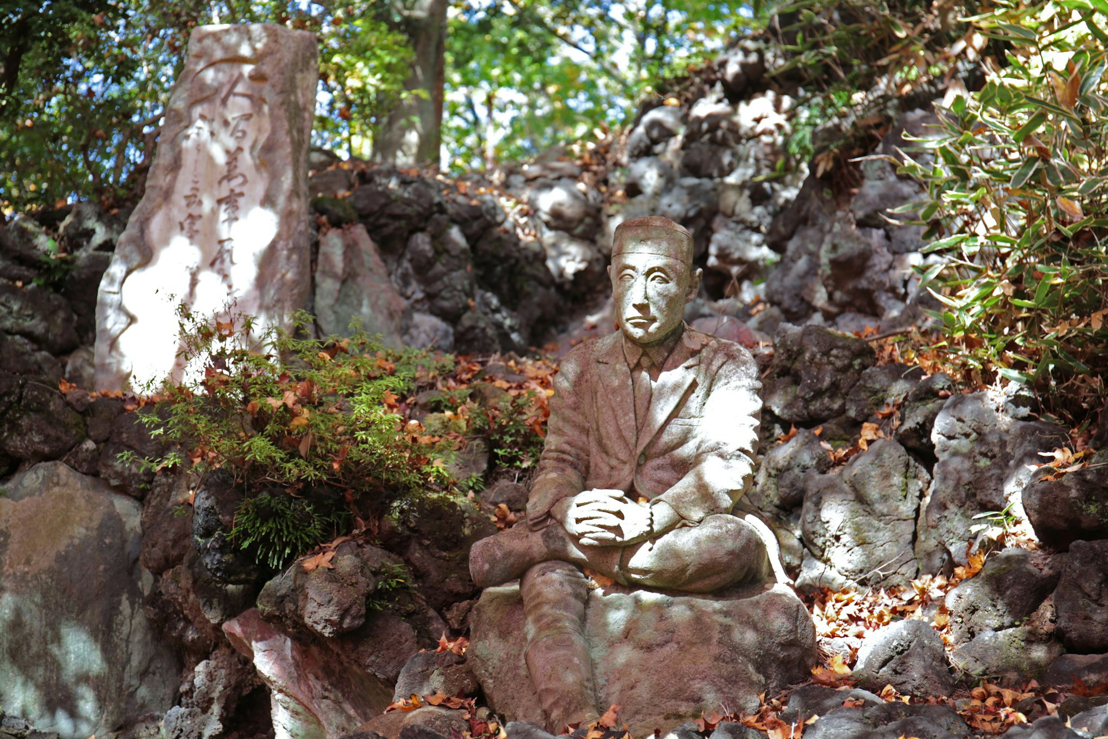 坐在岩石上的冥想雕塑，周围是绿色植物和落叶