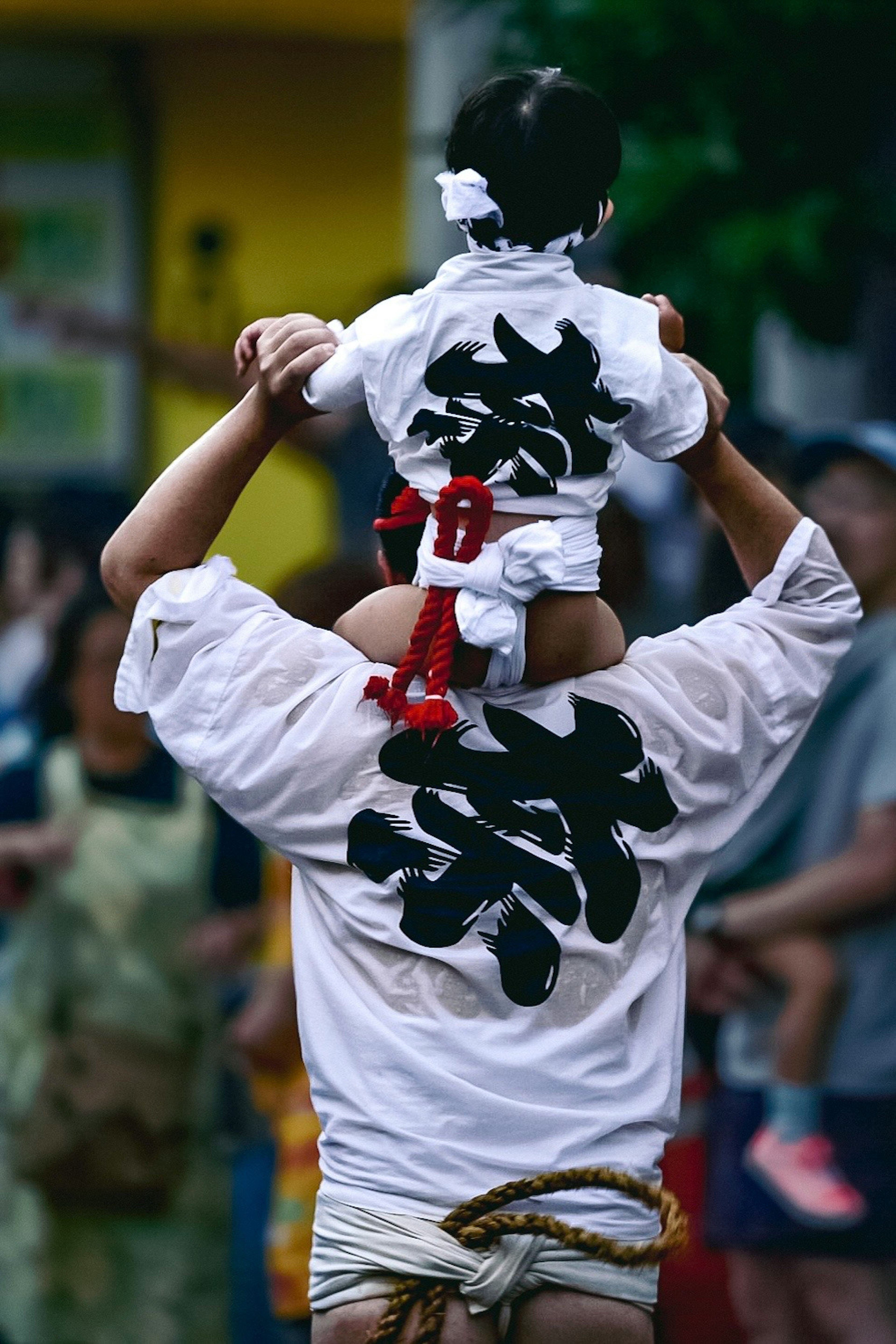 Parent carrying child on shoulders wearing traditional festival attire