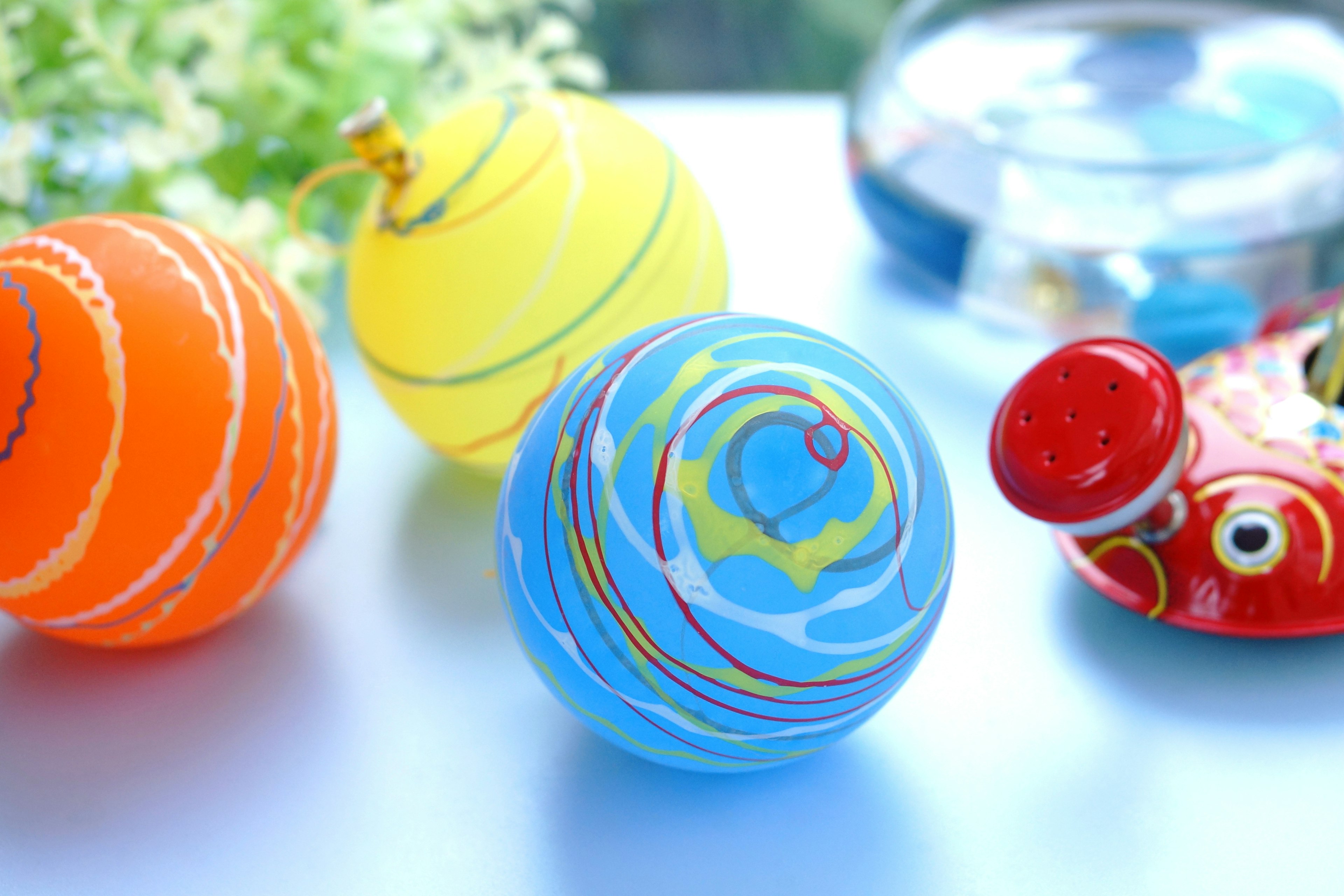 Colorful glass balls displayed on a surface Blue ball features wave patterns Yellow and orange balls are also present