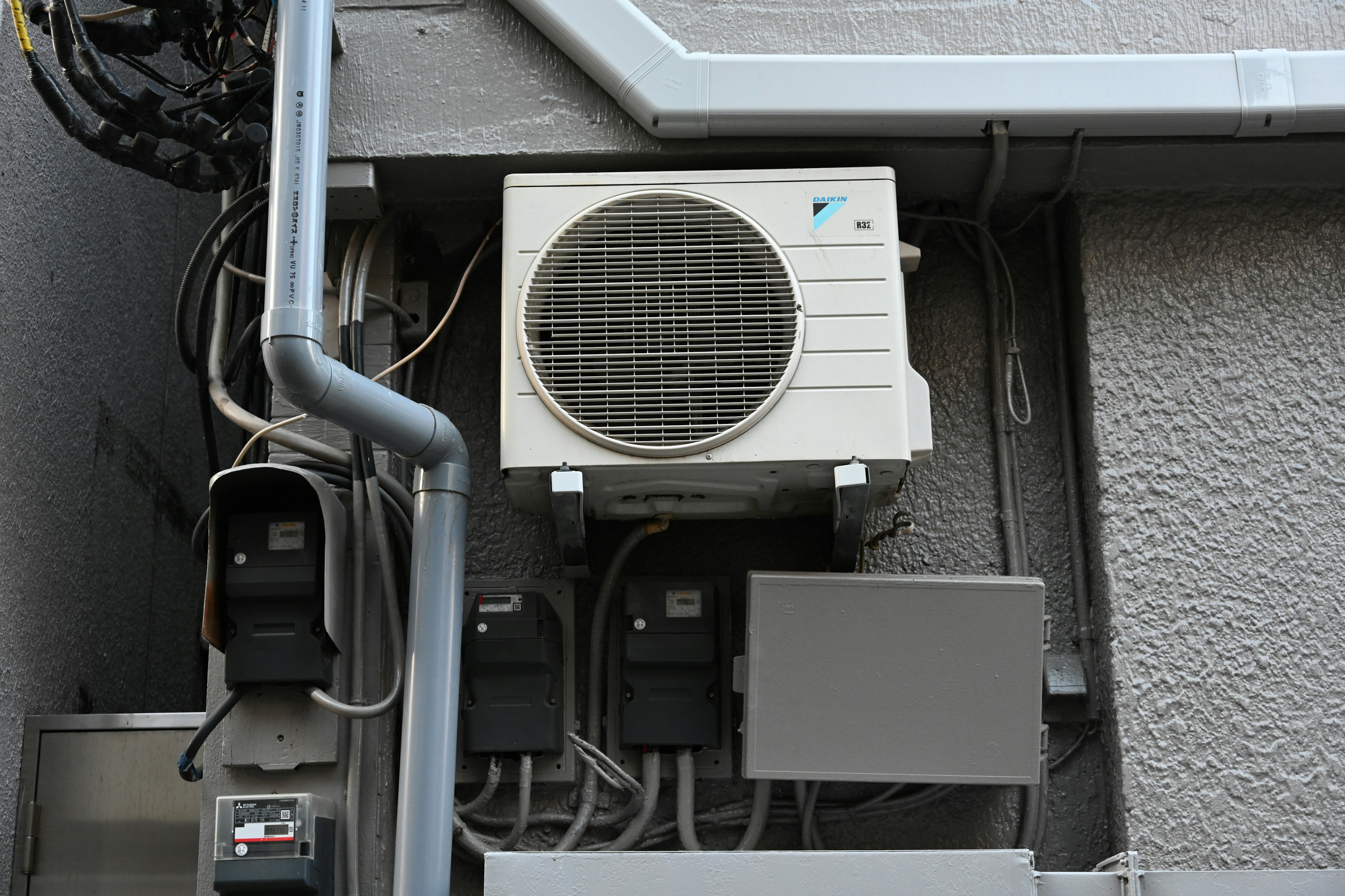 An air conditioning unit mounted on a wall with visible wiring and meters