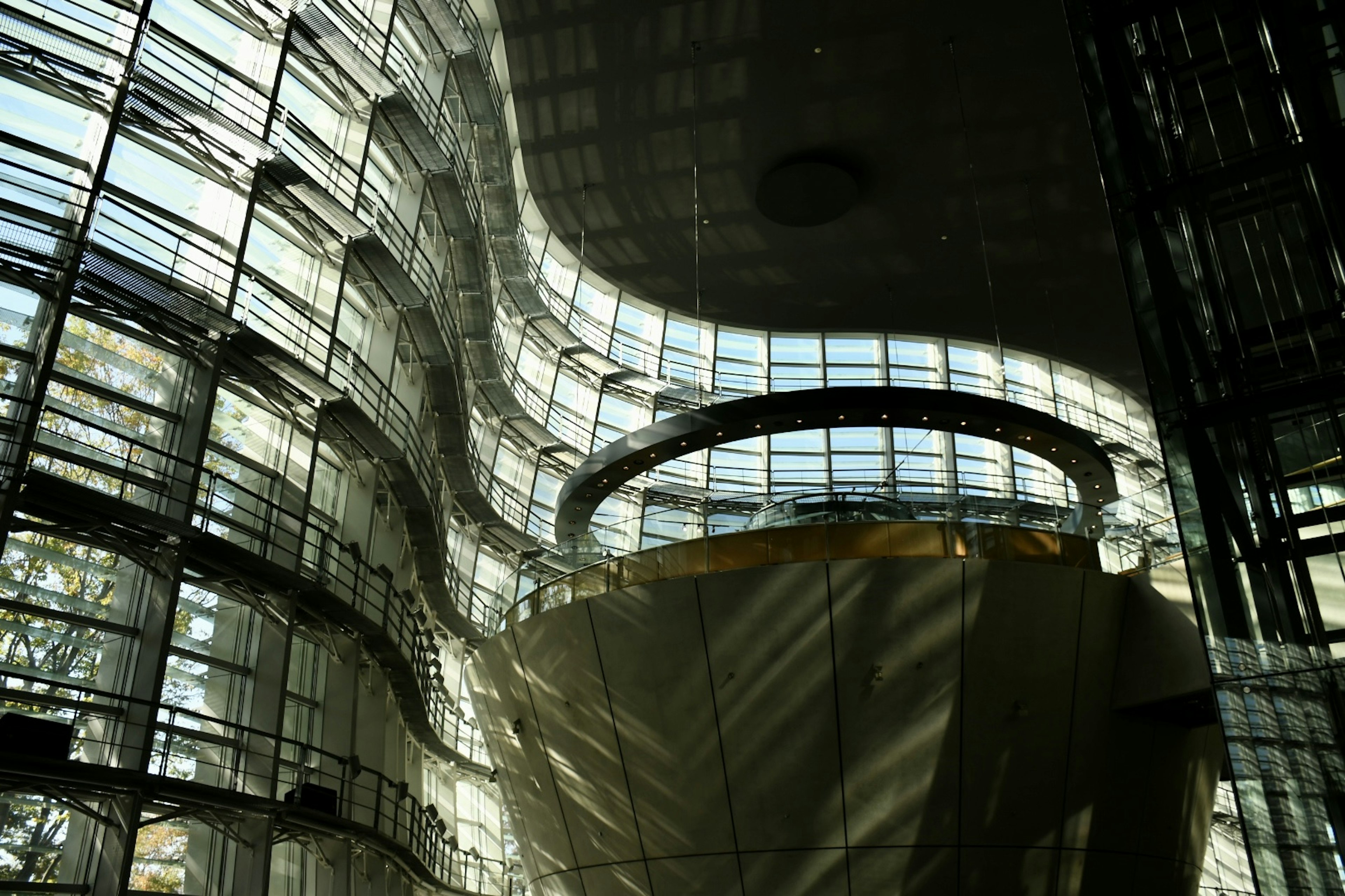 Intérieur d'un bâtiment moderne avec des murs en verre courbés présentant des contrastes de lumière et d'ombre saisissants