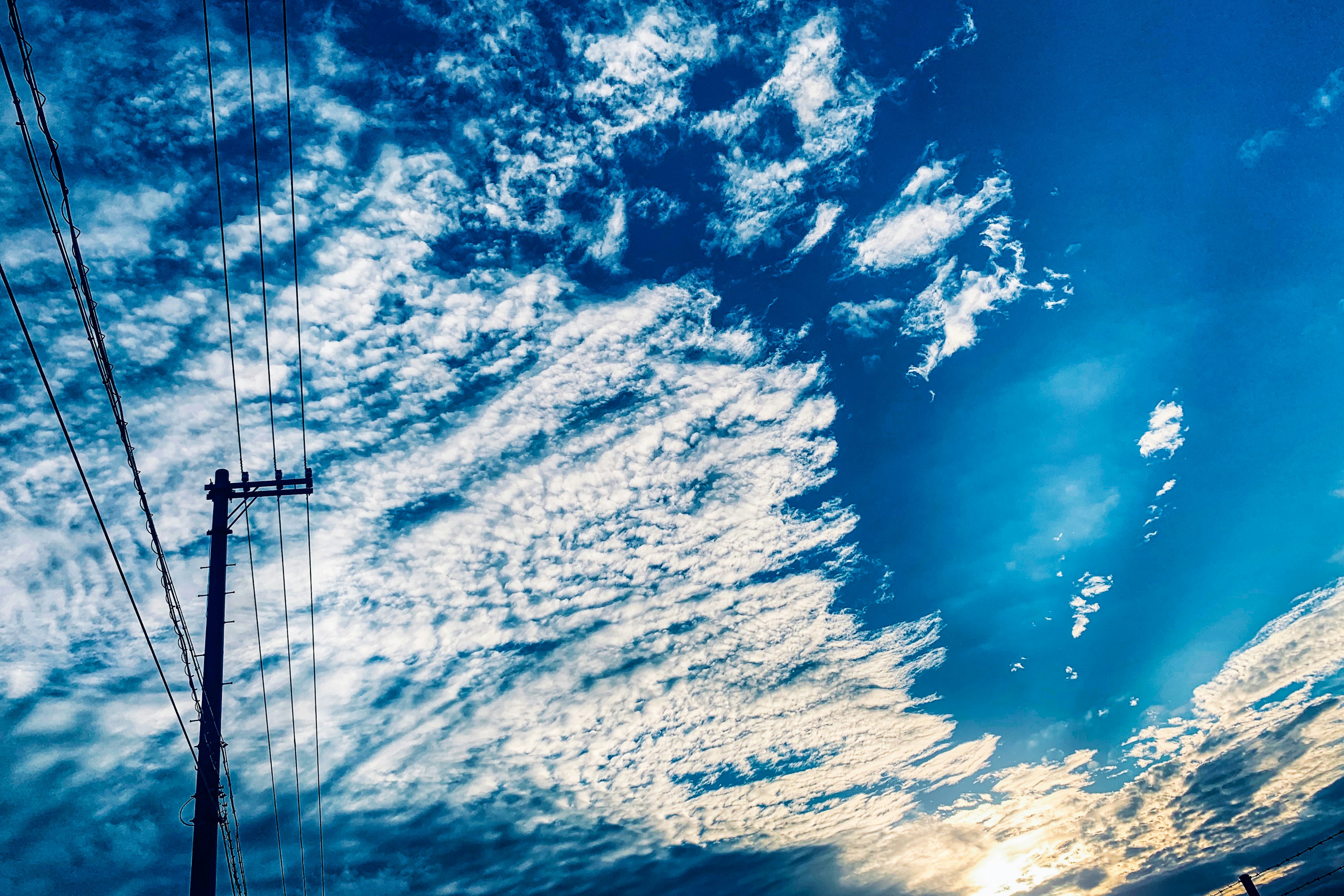 青空に広がる雲と電柱のシルエット