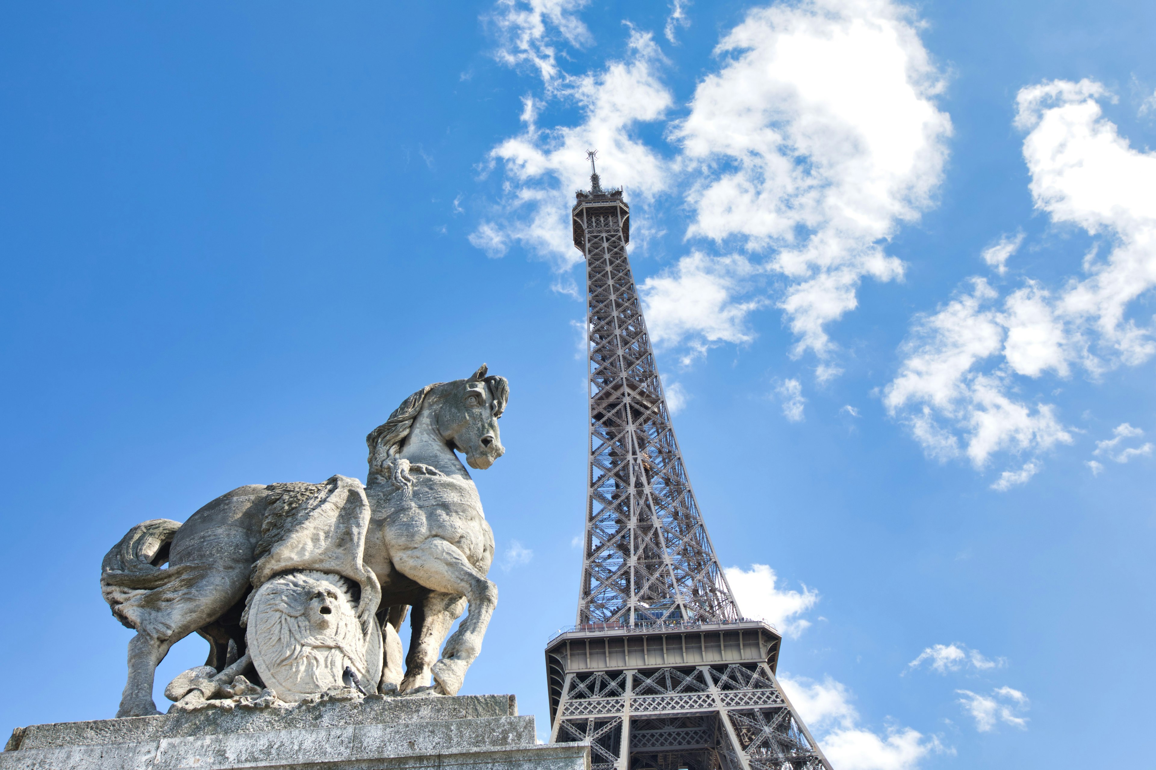 View of the Eiffel Tower with a horse sculpture under a blue sky