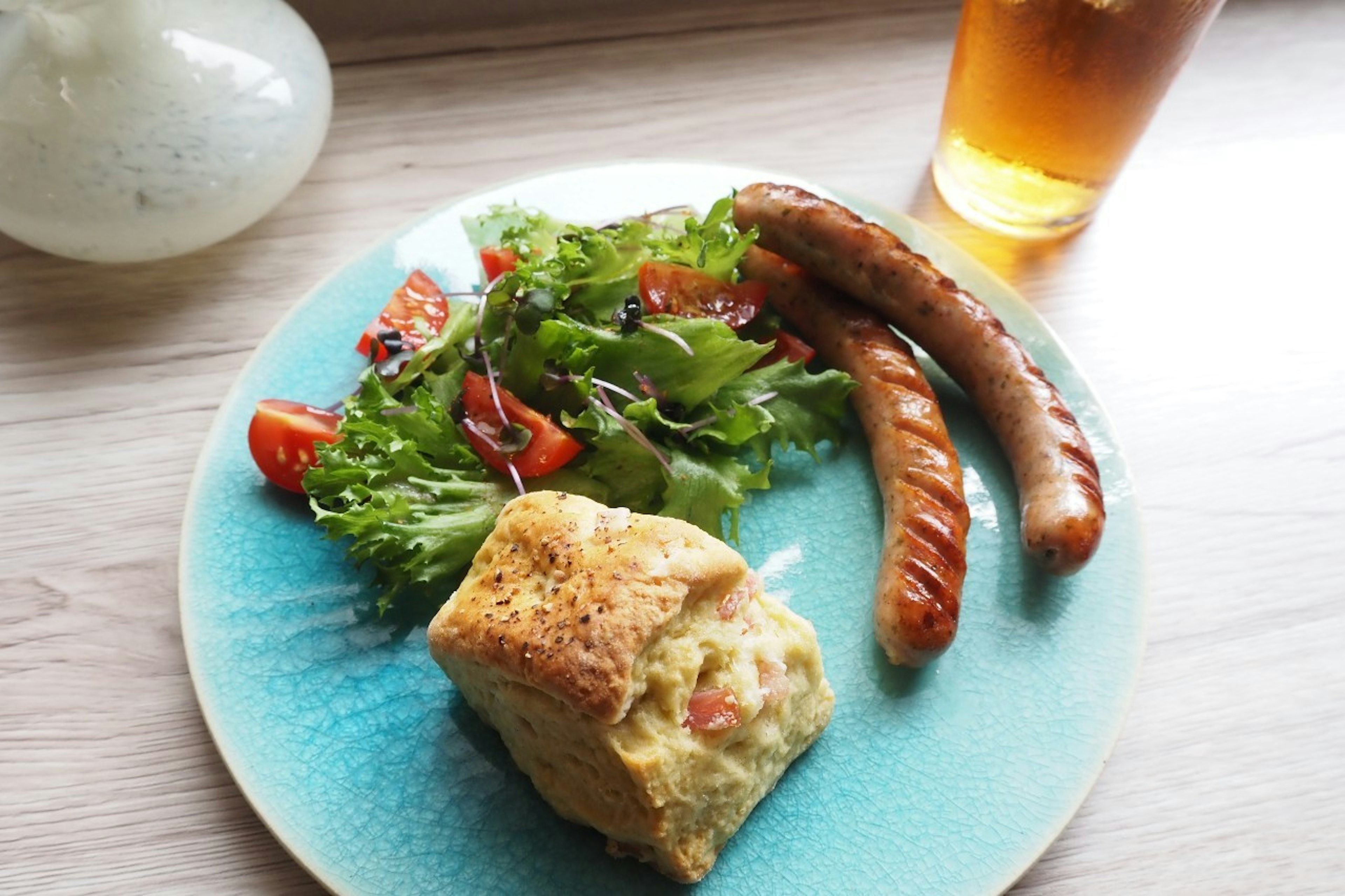 A blue plate featuring salad, sausages, and a baked good