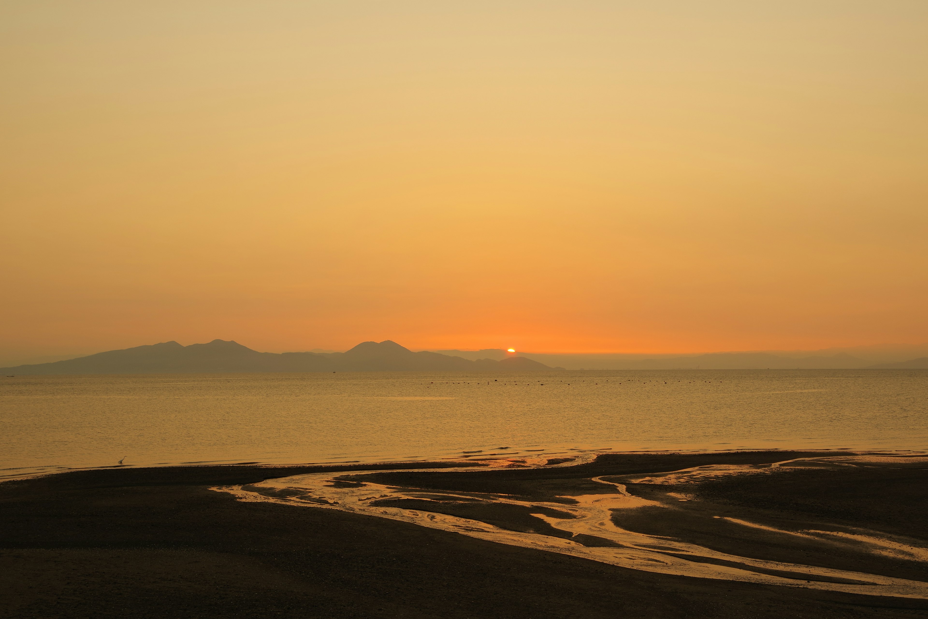 Sonnenuntergang über dem Meer mit Sandstrand und Flusslauf