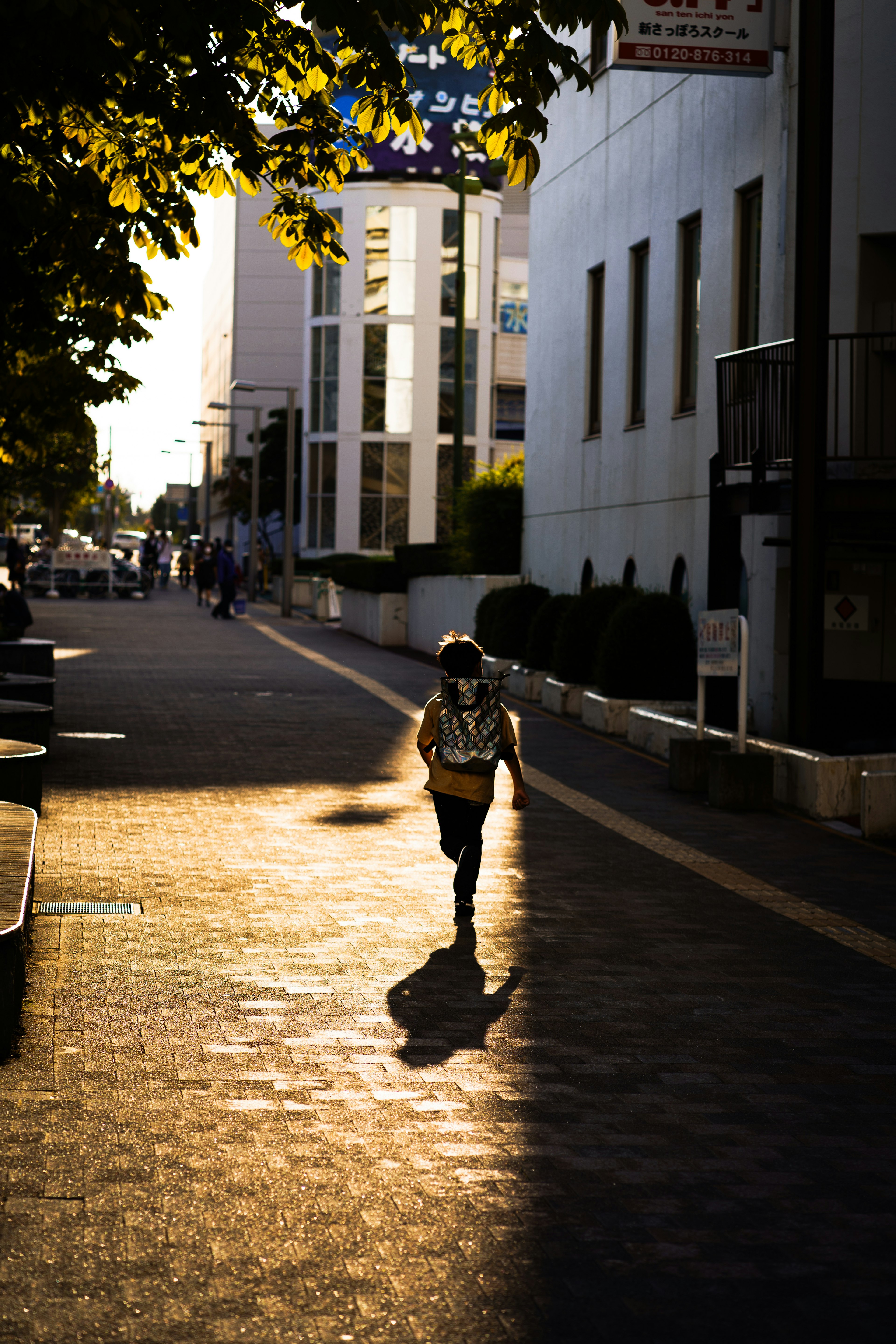 Silueta de una persona caminando en una calle iluminada por el atardecer con contraste de luz cálida