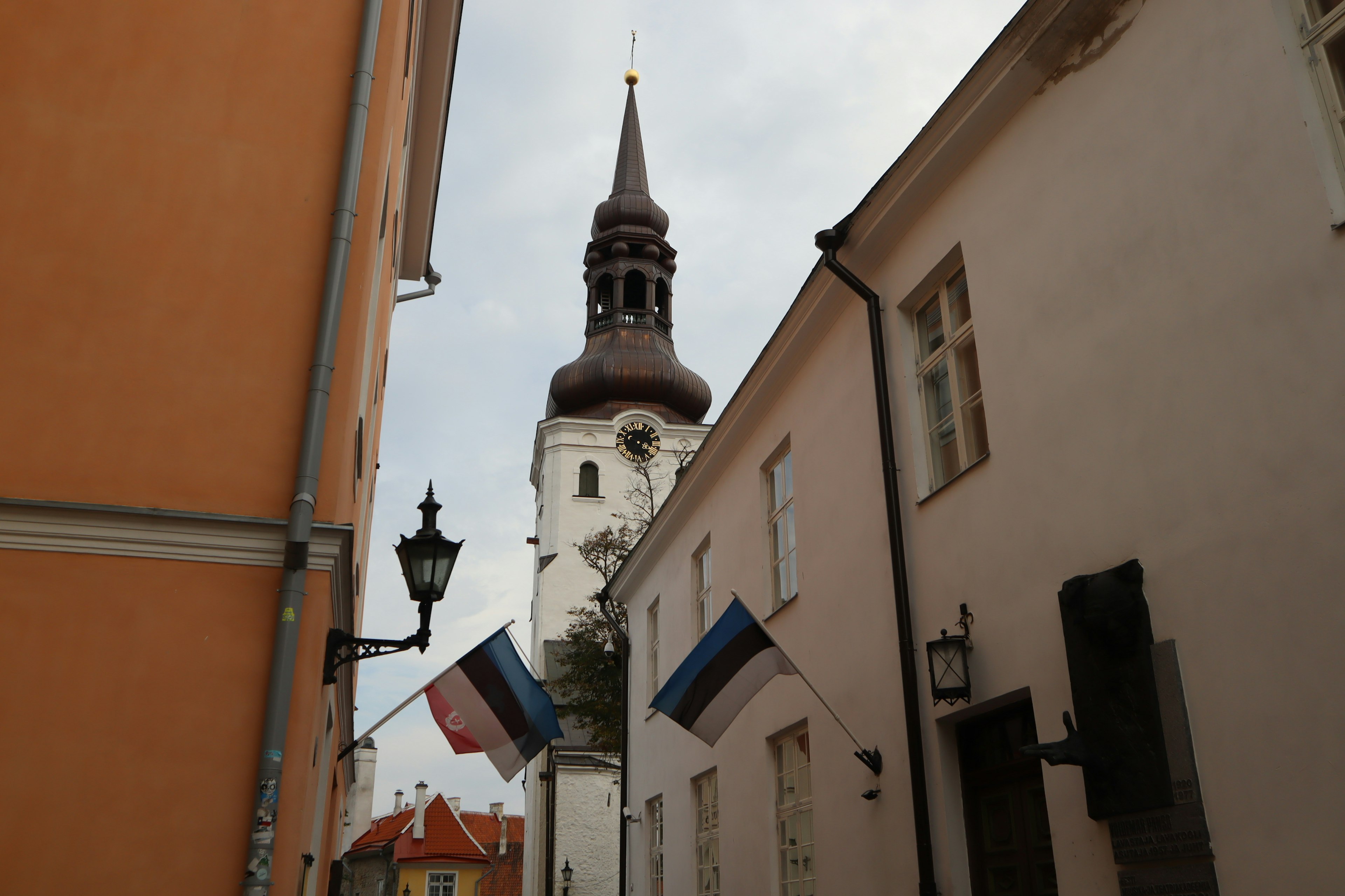 Narrow street in Tallinn Estonia featuring church tower and flags