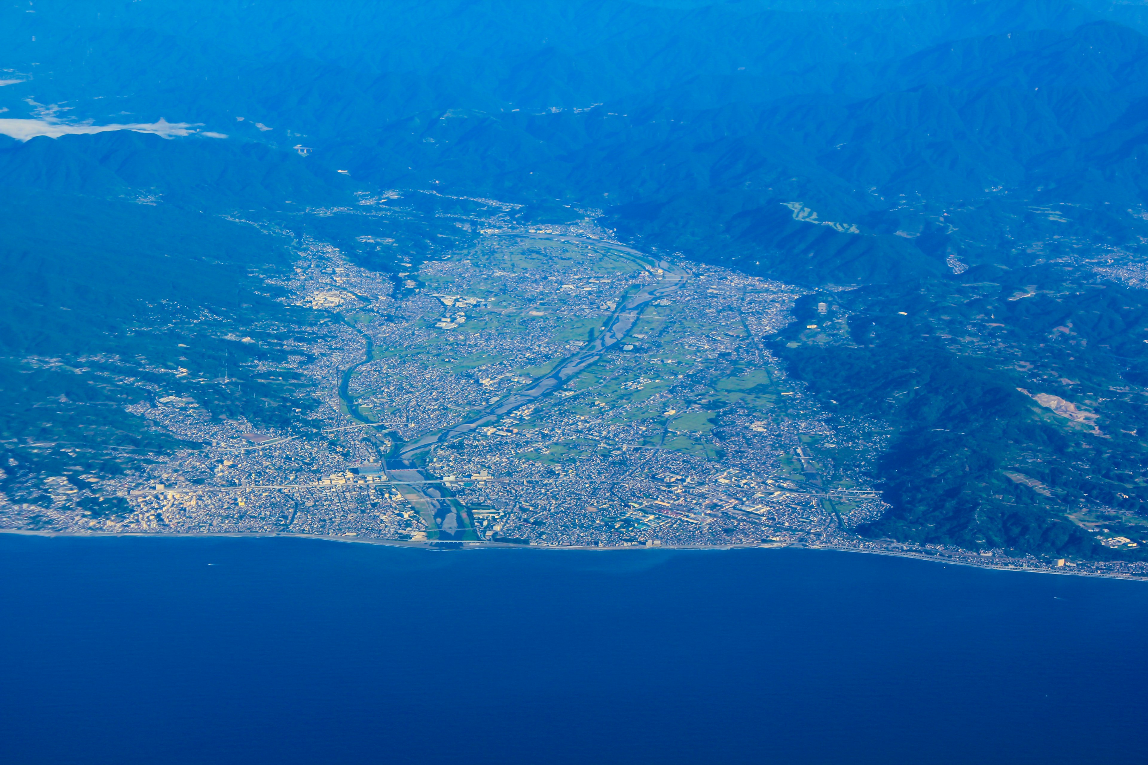 Luftaufnahme einer Küstenstadt mit blauem Ozean und Bergen im Hintergrund