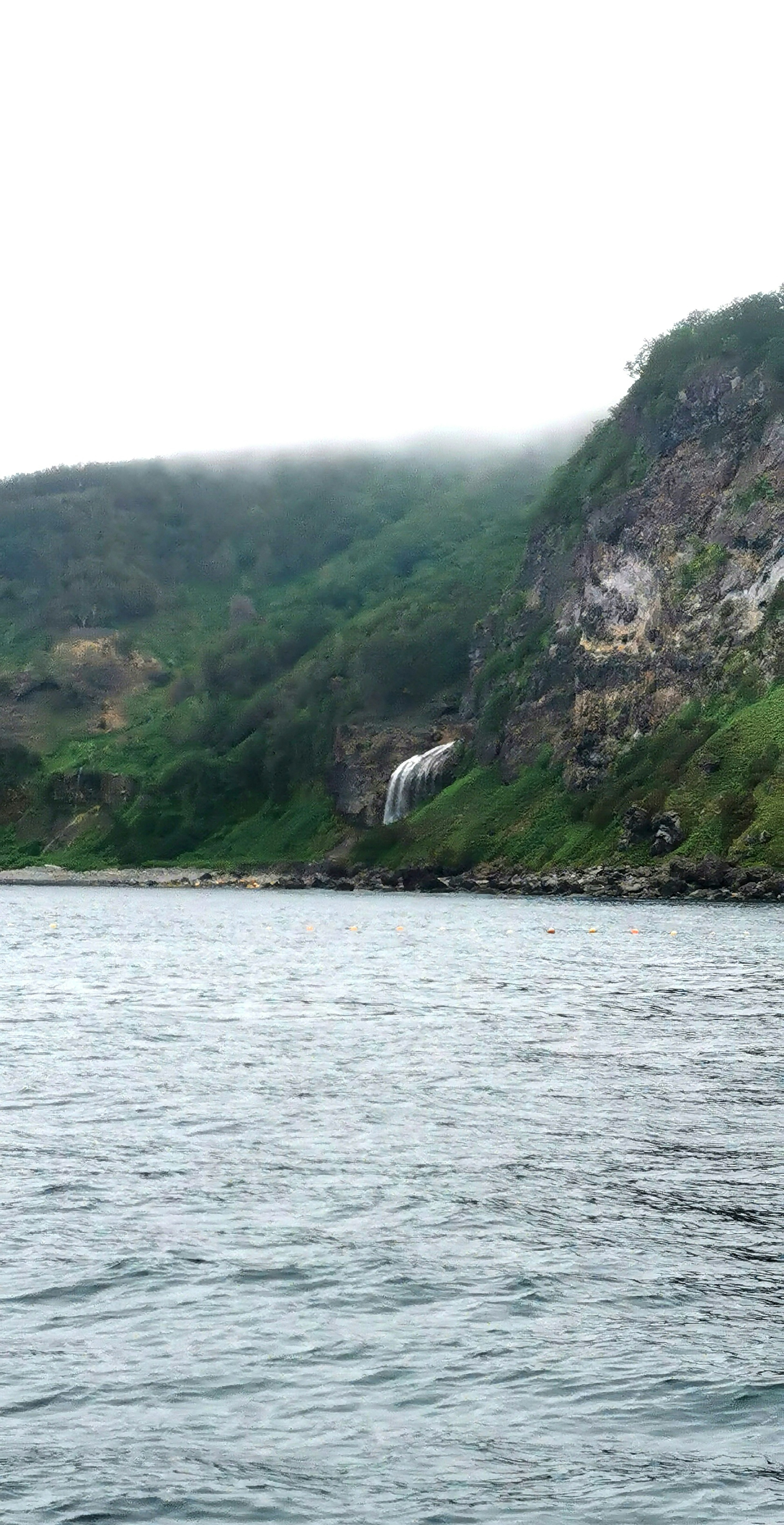 Malersicher Blick auf einen Wasserfall, der an einem nebligen Hang am Meer herabfällt